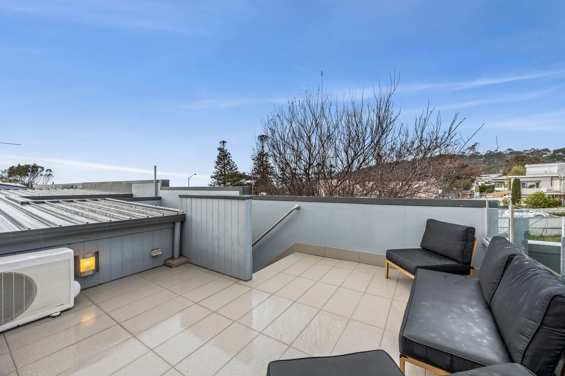 A rooftop terrace has tiled flooring, outdoor seating, and a view of nearby rooftops.