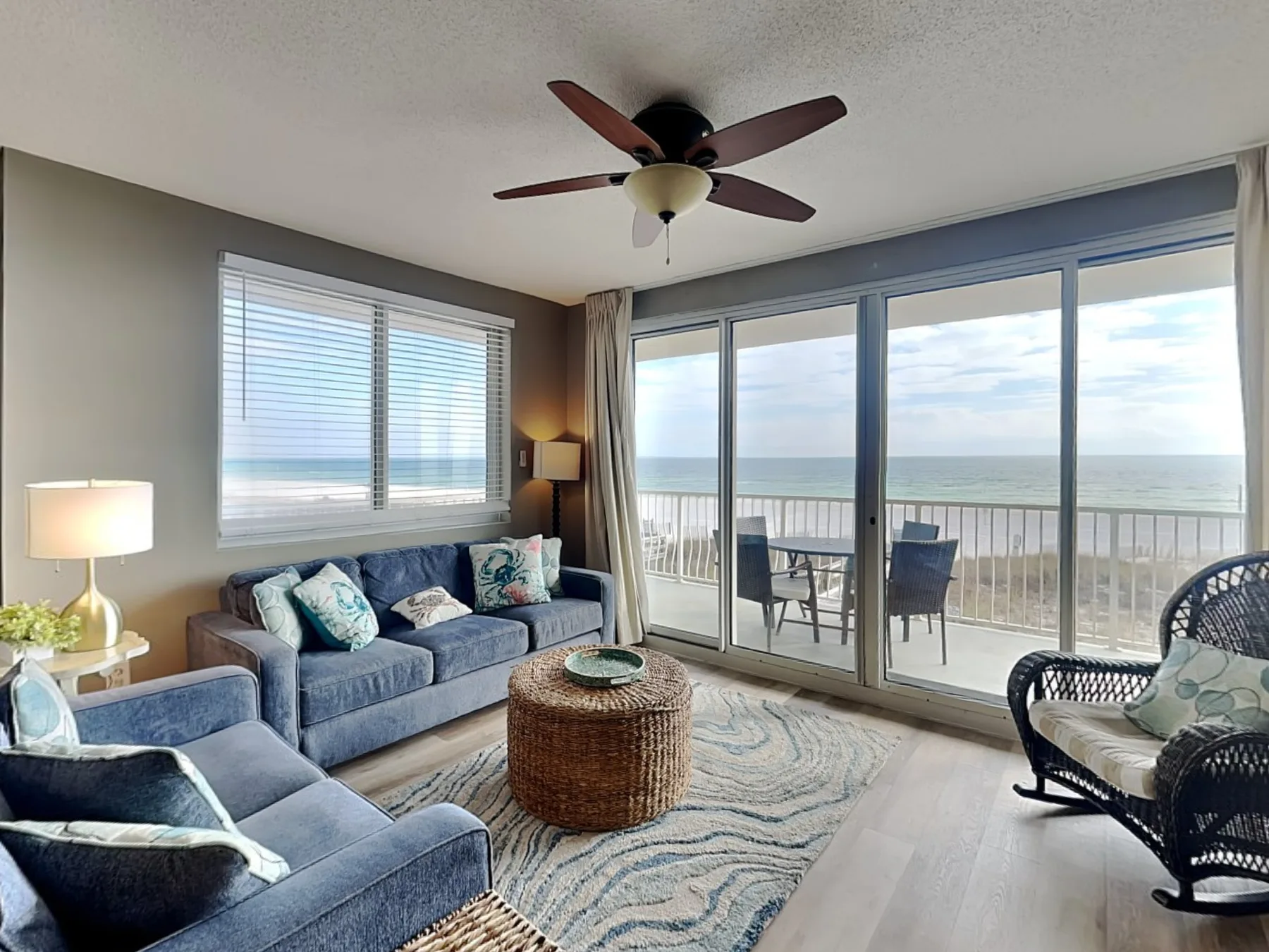 A living room with blue seating and large windows overlooking the ocean.