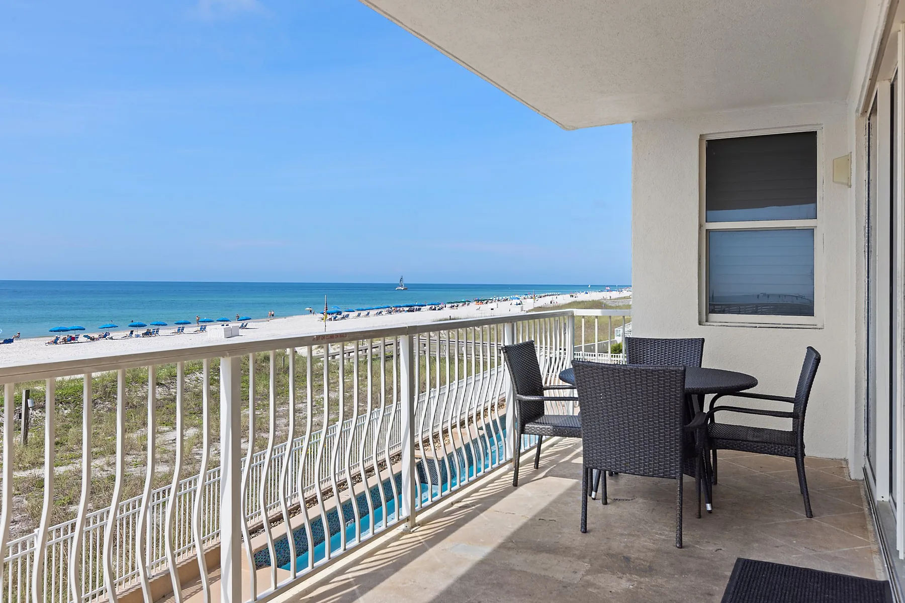 A balcony overlooking the beach and ocean, with an outdoor dining table and seating.
