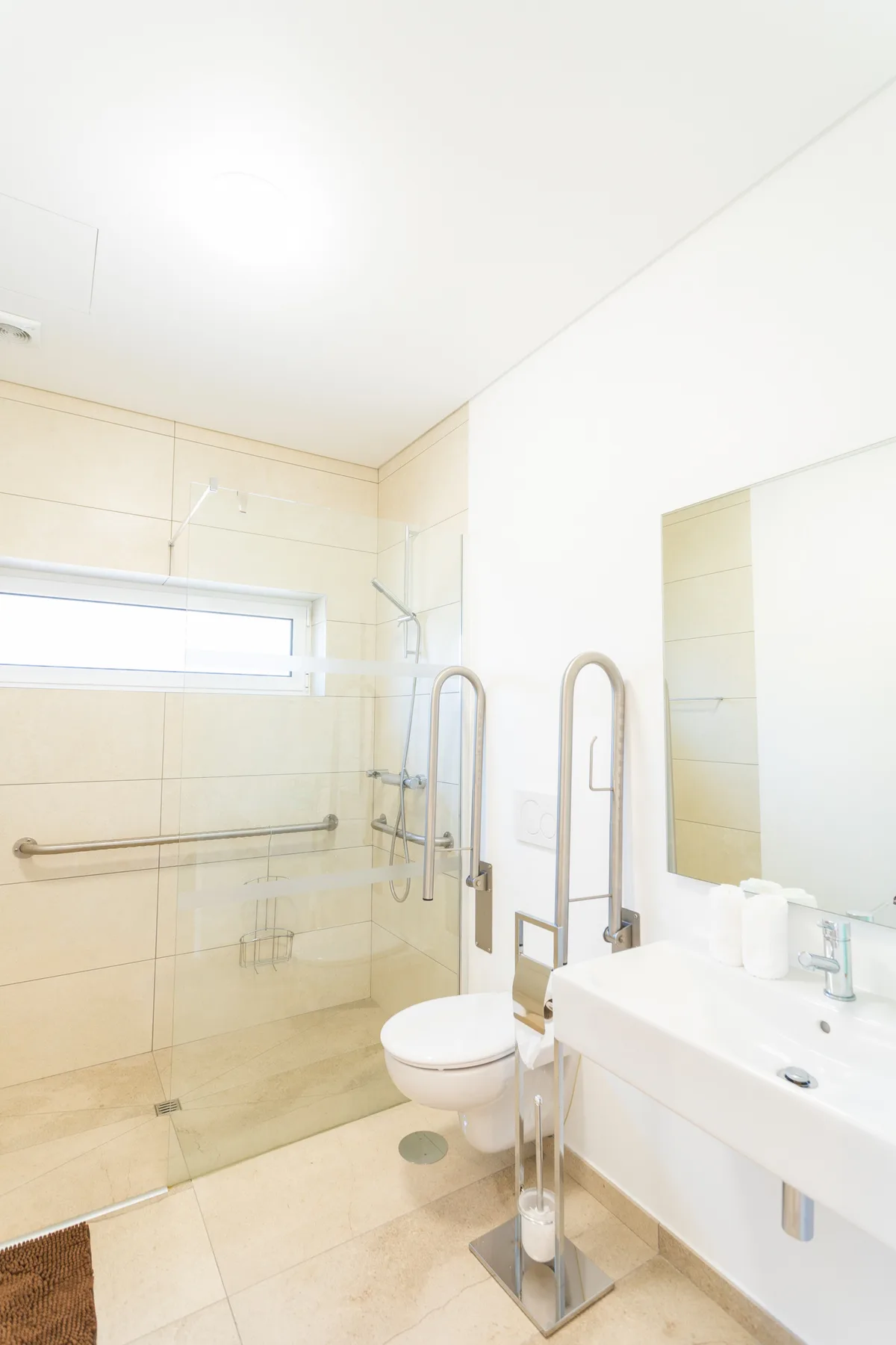 A bright tiled bathroom with a glass shower, toilet, and sink.