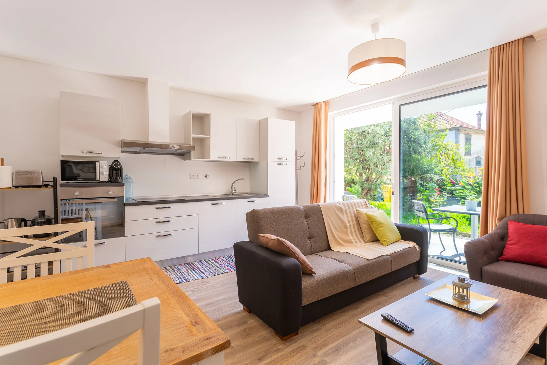 An open-plan living room and kitchen with a dining table beside glass doors.