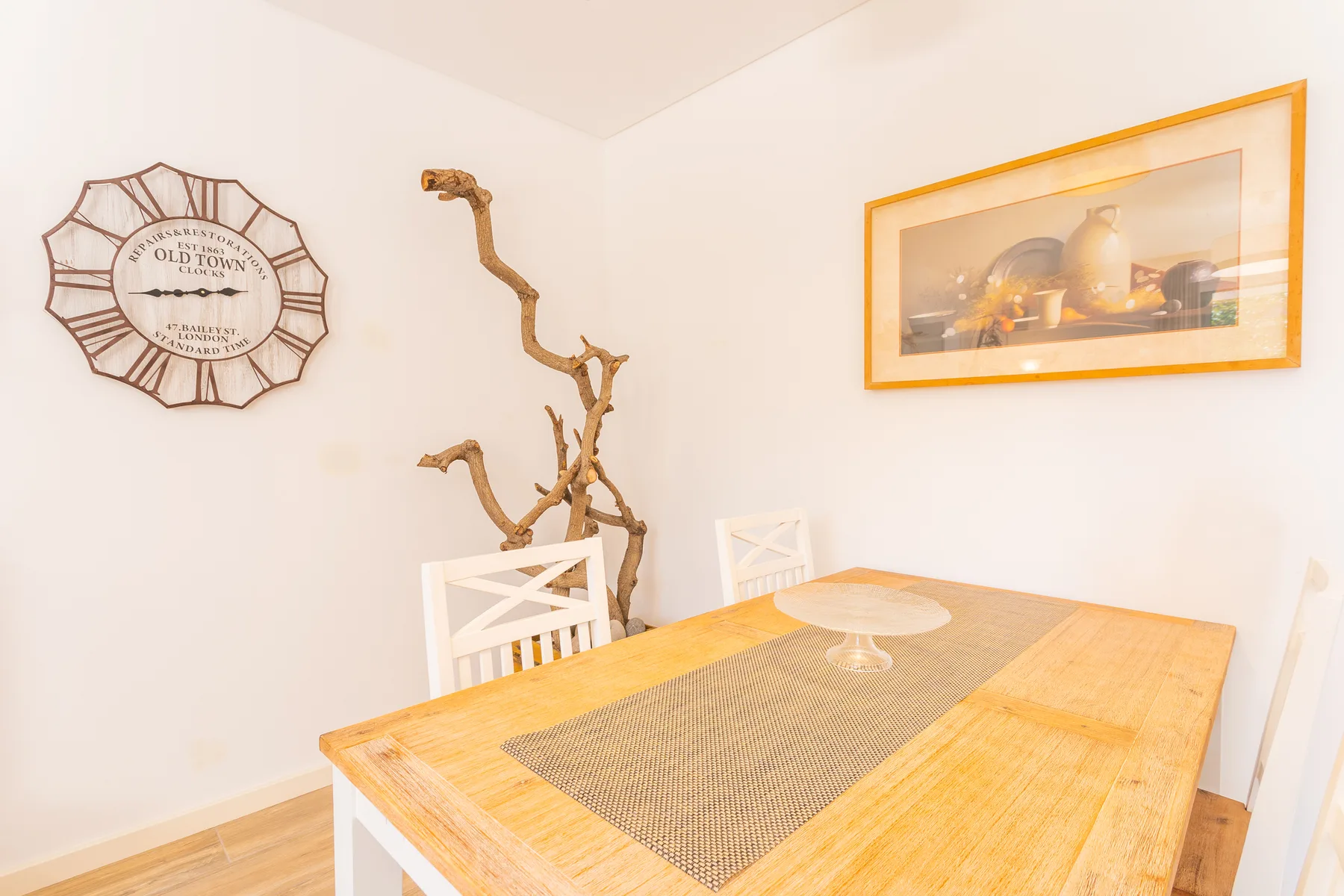 A dining area with a wooden table, woven runner, and framed wall art.