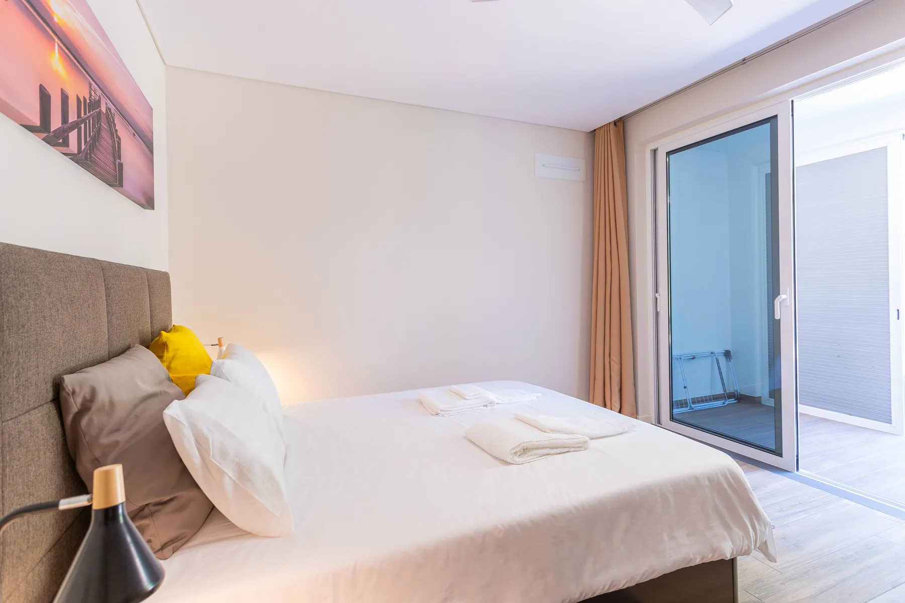 A bright bedroom with a neatly made bed beside sliding glass doors.