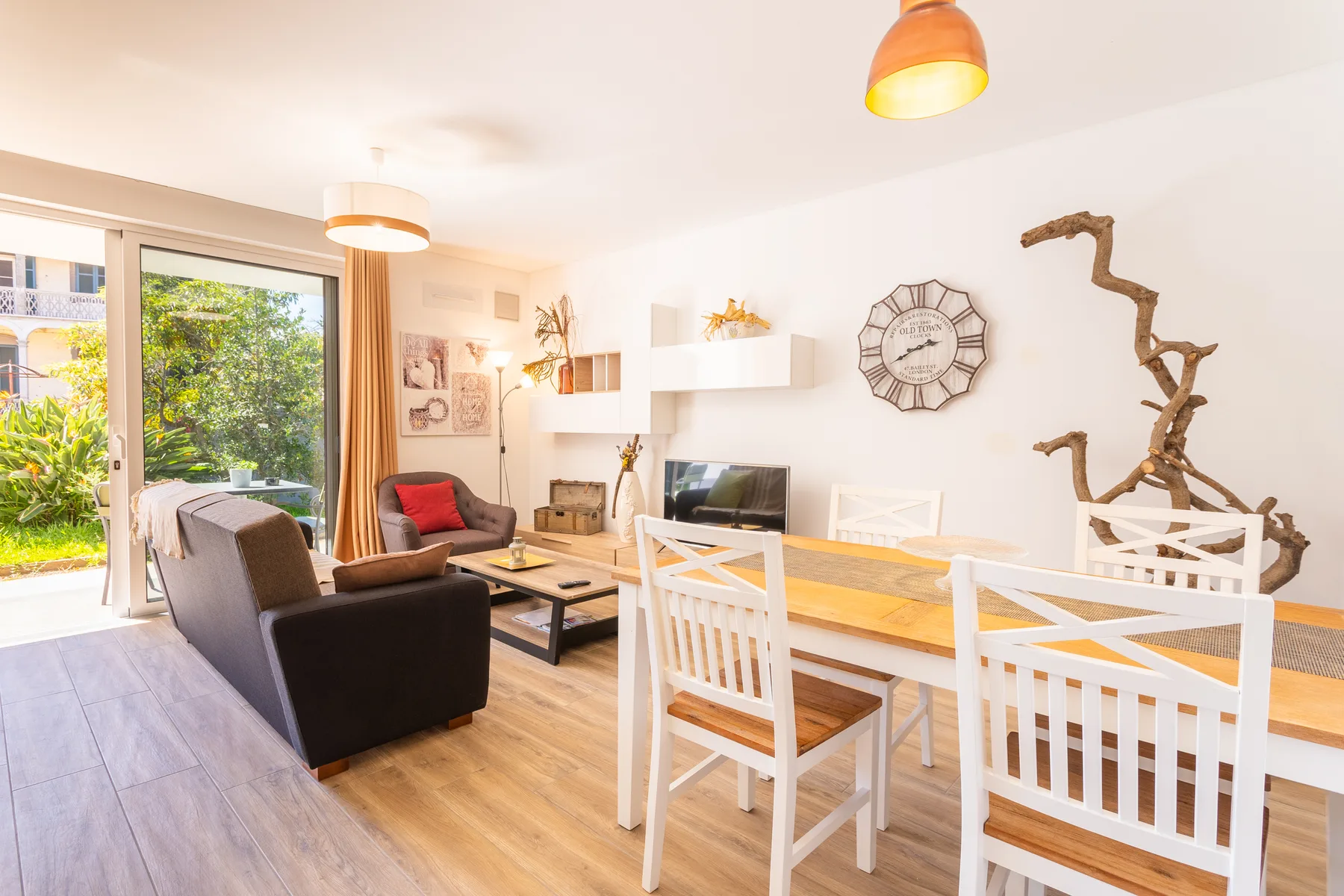 A bright living and dining area with seating, a television, and a glass door opening to greenery.