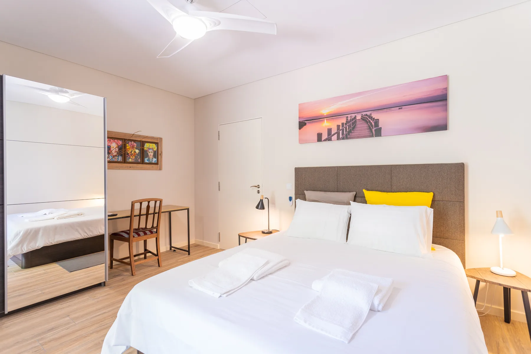 A bright bedroom with a neatly made bed and framed artwork above the headboard.