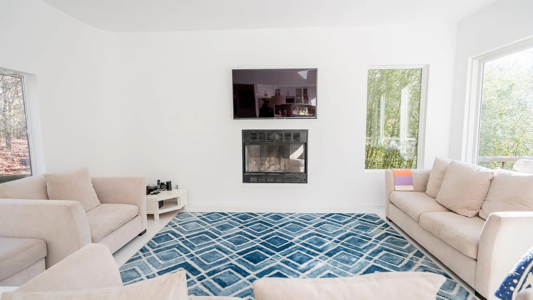 A bright living room with seating, a blue patterned rug, and a wall-mounted television.