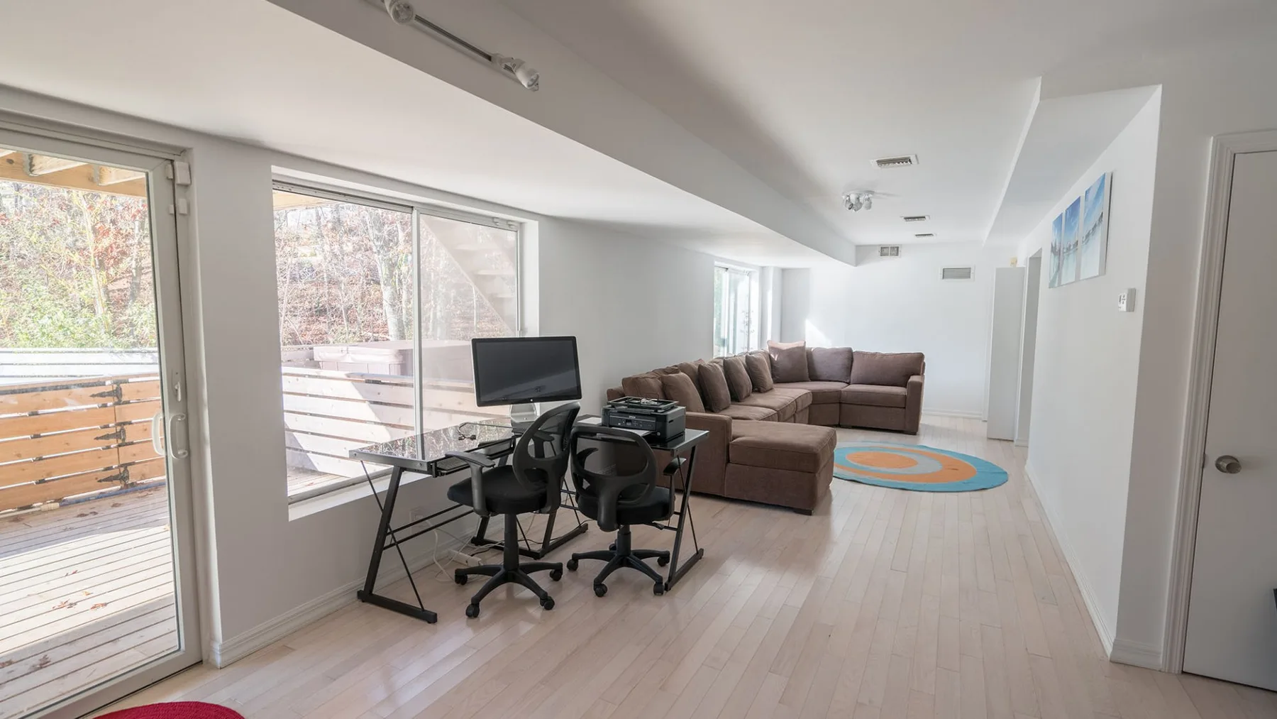 A bright living room with a sectional seating area and a desk by the windows.