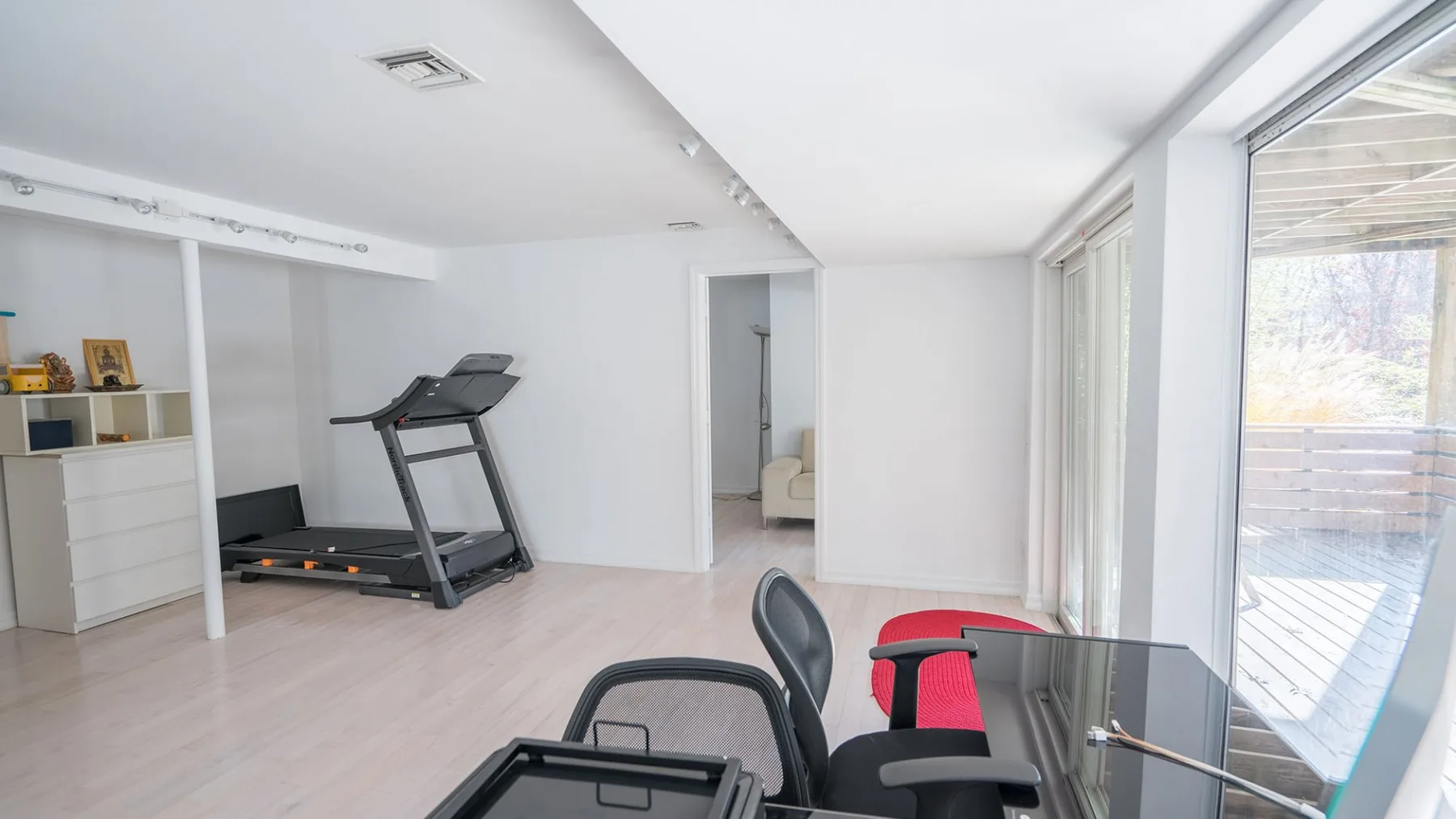 A bright exercise room with a treadmill and large windows.