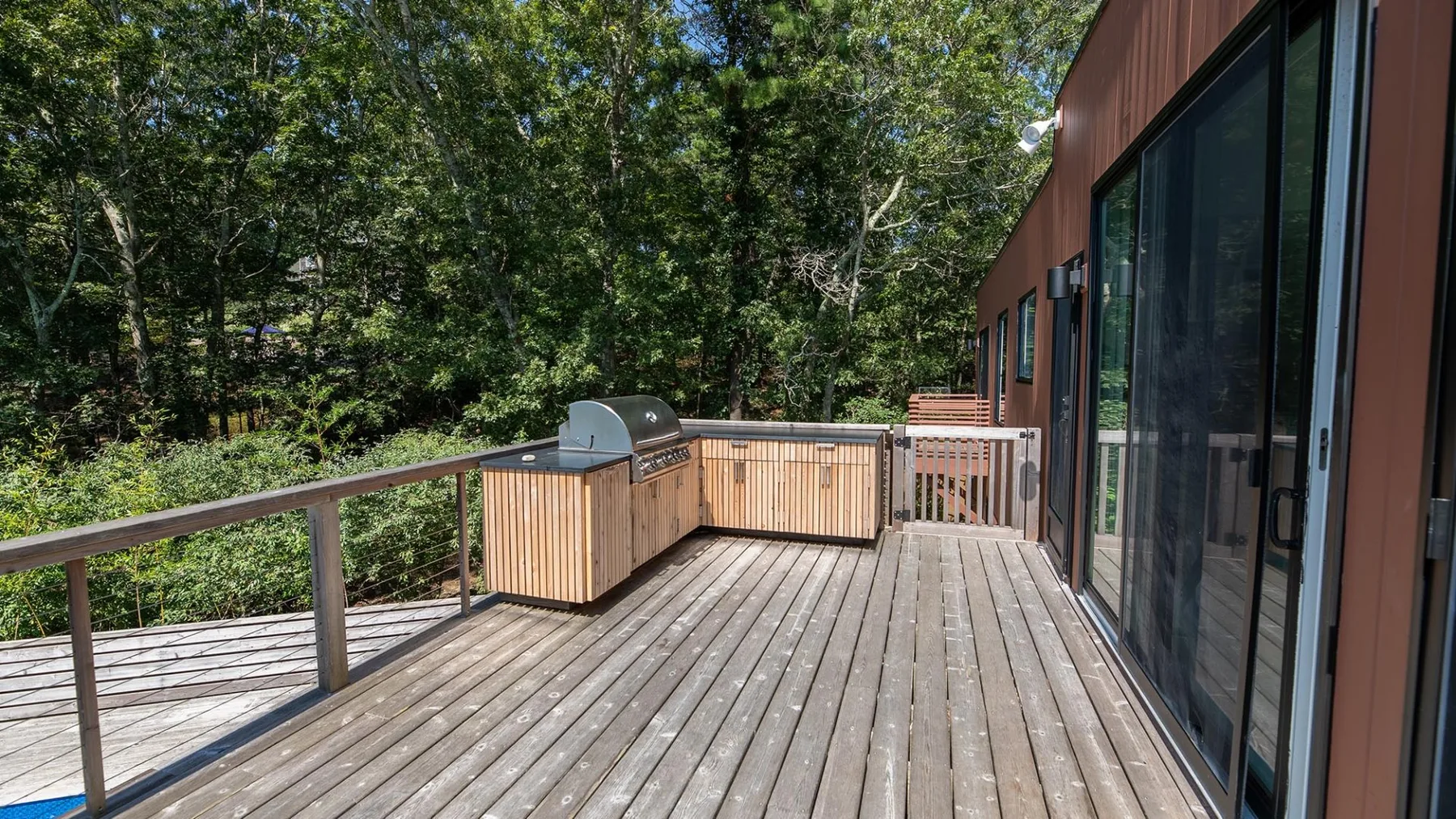 A wooden deck beside a building, with trees visible beyond the railing.