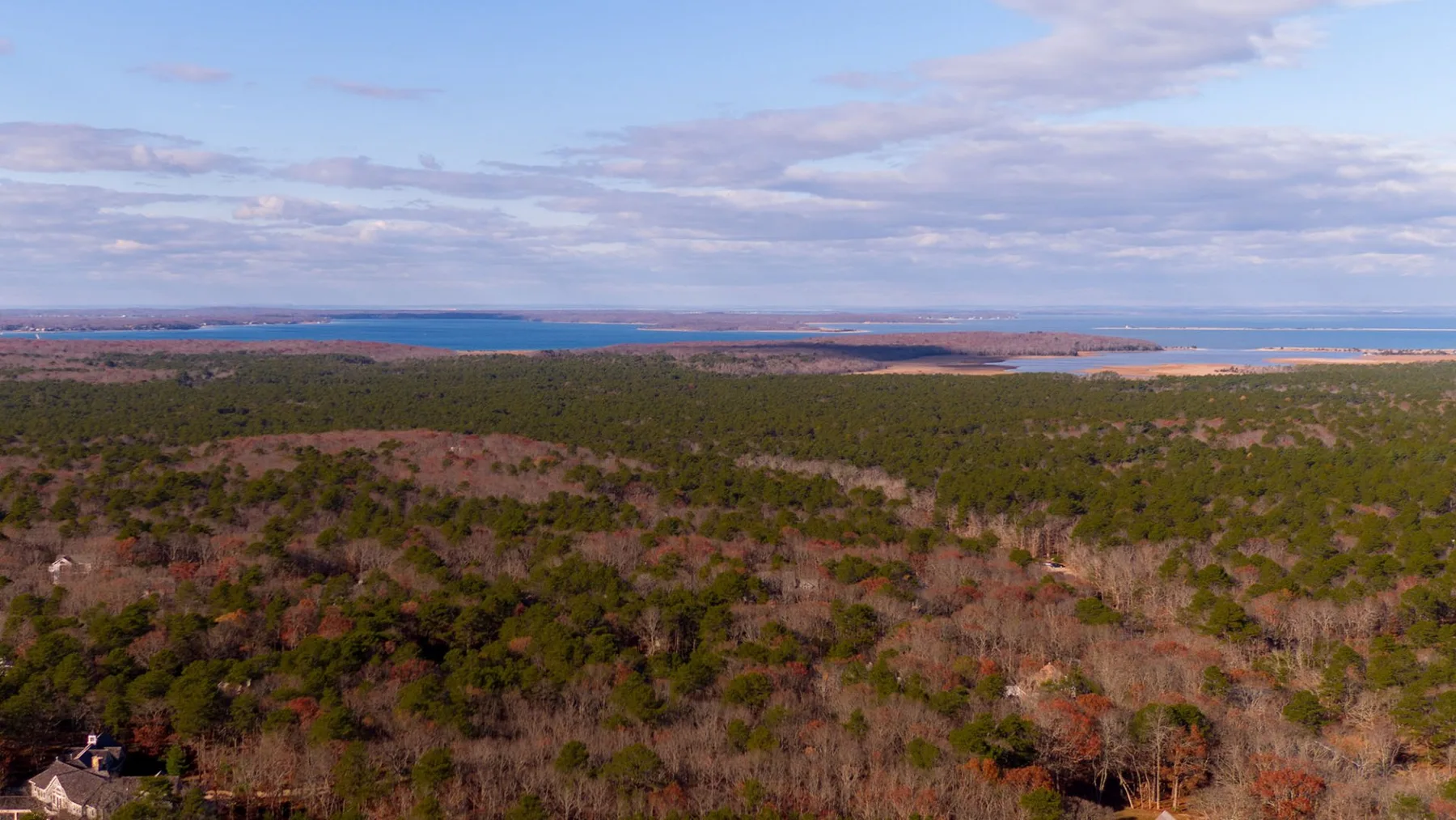 Aerial view of a broad forested landscape beneath a partly cloudy sky.