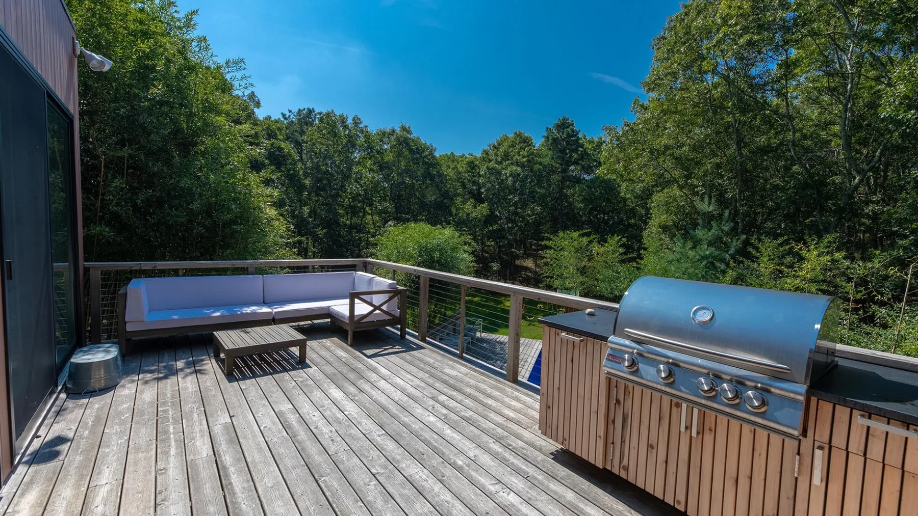 A wooden deck overlooks leafy trees, with outdoor seating and a built-in grill.