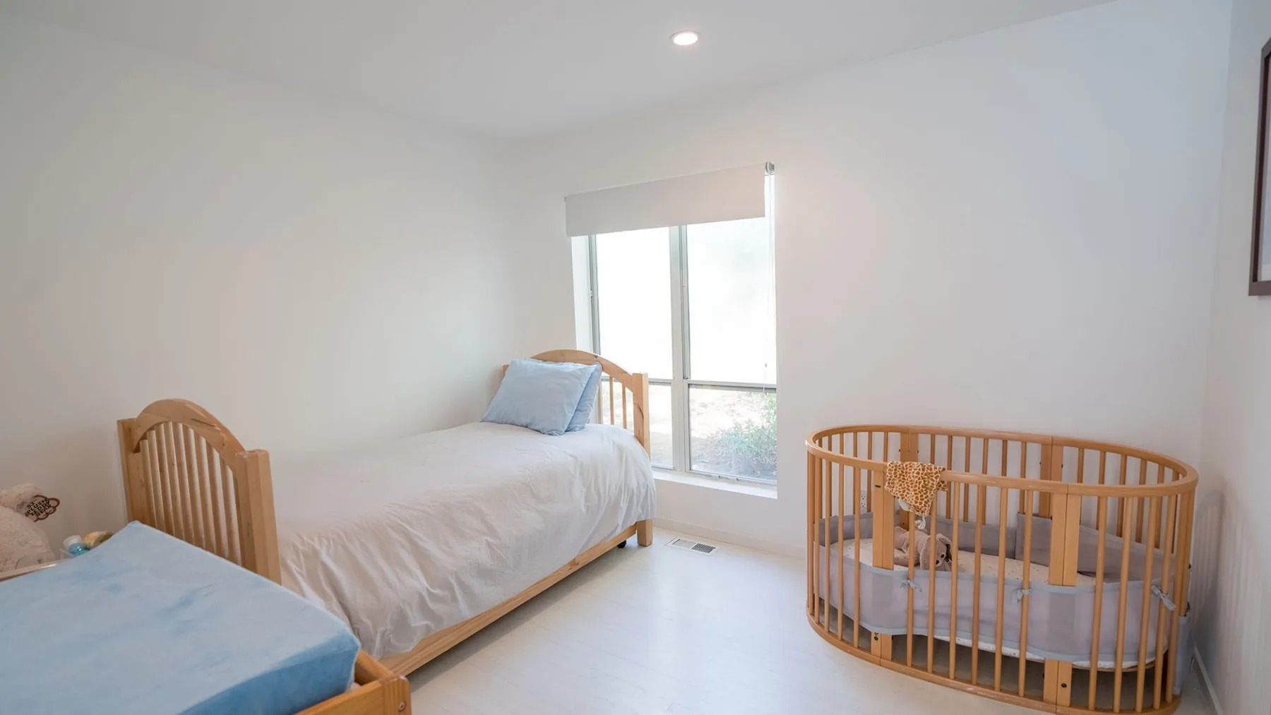 A bright bedroom with two single beds and a wooden crib beside the window.