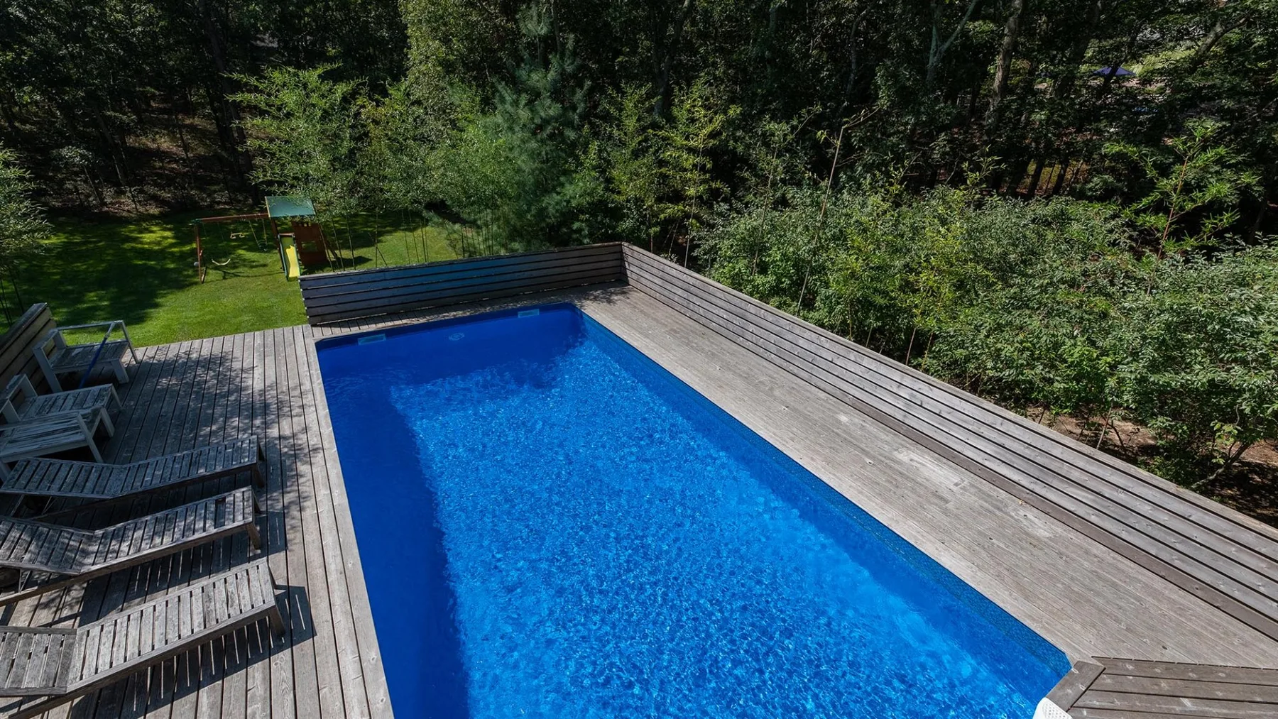 An outdoor swimming pool is surrounded by a wooden deck and trees.