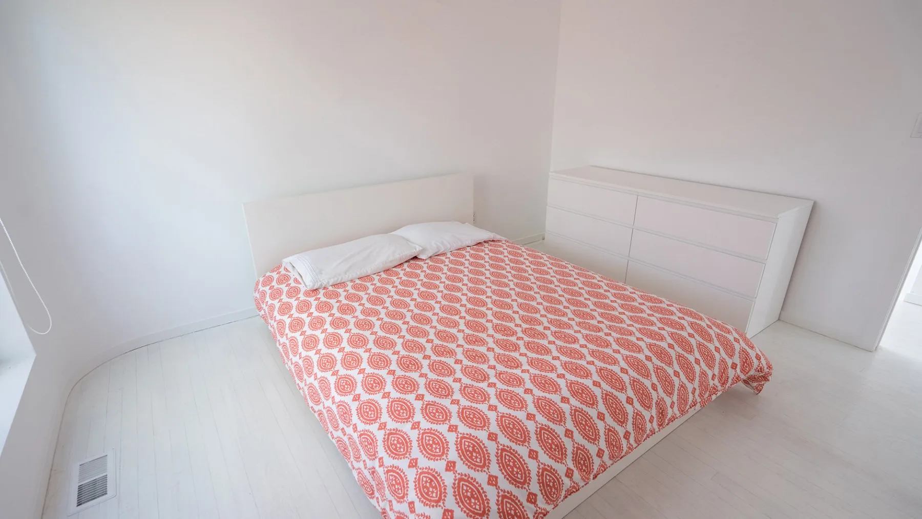 A bedroom with a bed covered by a red-and-white patterned bedspread.