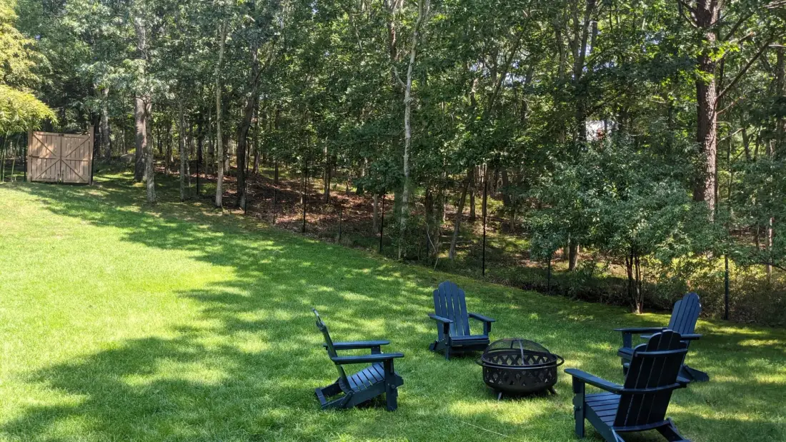 A grassy outdoor seating area with chairs and a fire pit near the trees.
