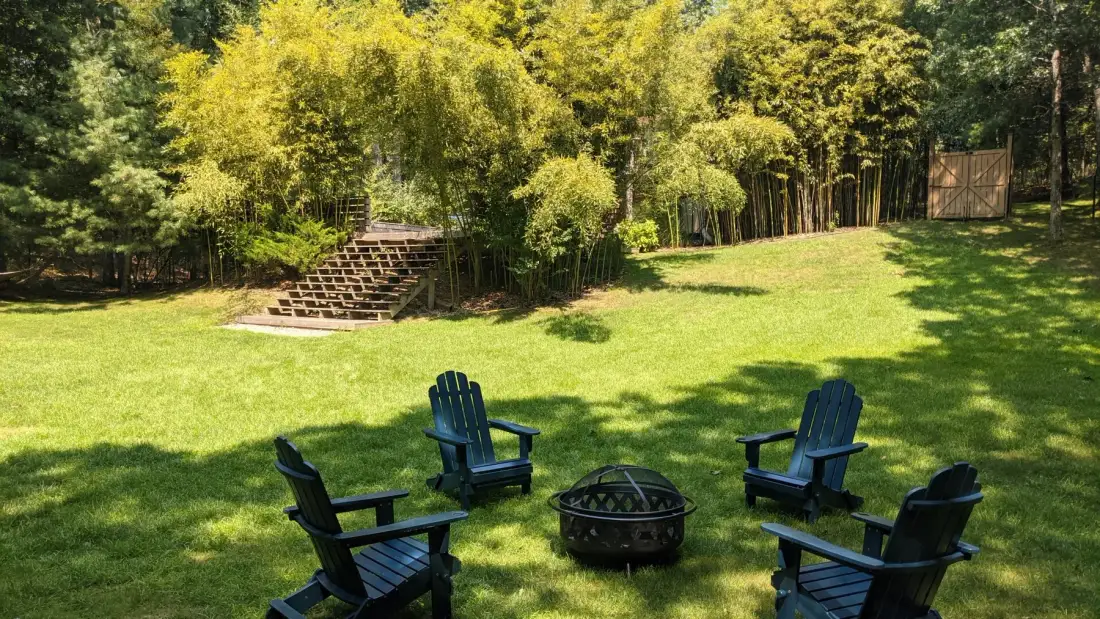 A grassy outdoor seating area with chairs around a fire pit.