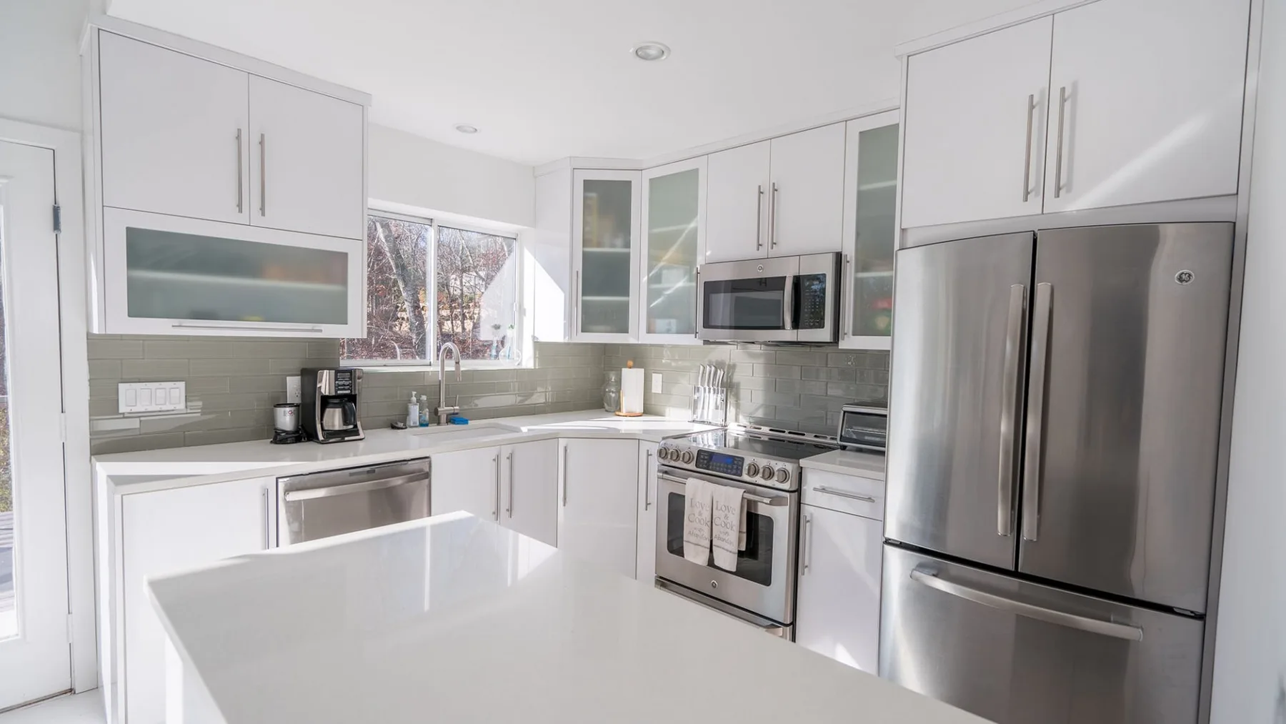 A bright modern kitchen with white cabinets and stainless steel appliances.