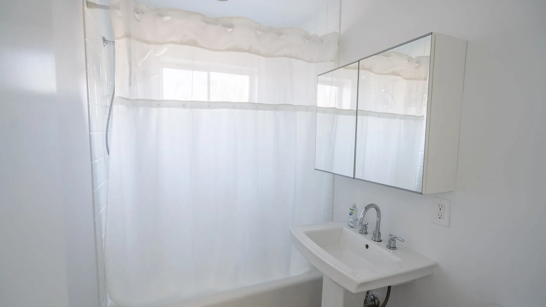 A bathroom with a sink, mirrored cabinet, and shower curtain.