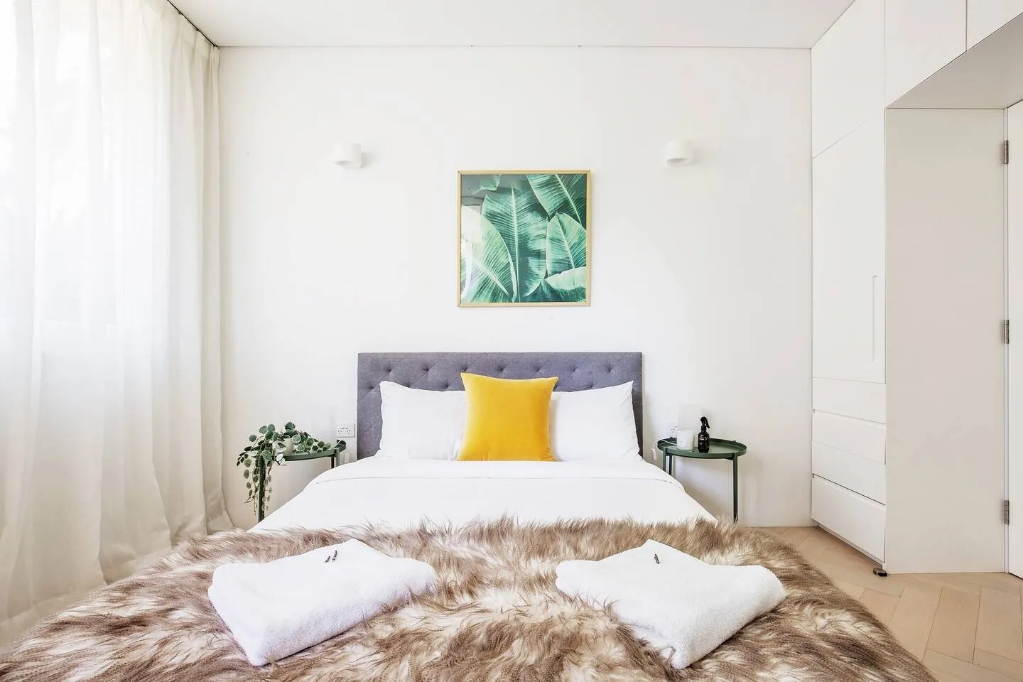 Un dormitorio luminoso tiene una cama con ropa de cama blanca y un cojín amarillo.