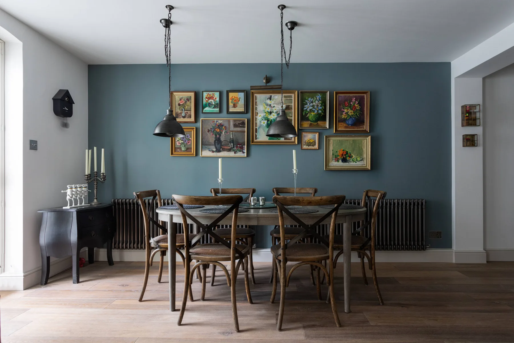 A dining room with a wooden table and framed artwork on a blue wall.