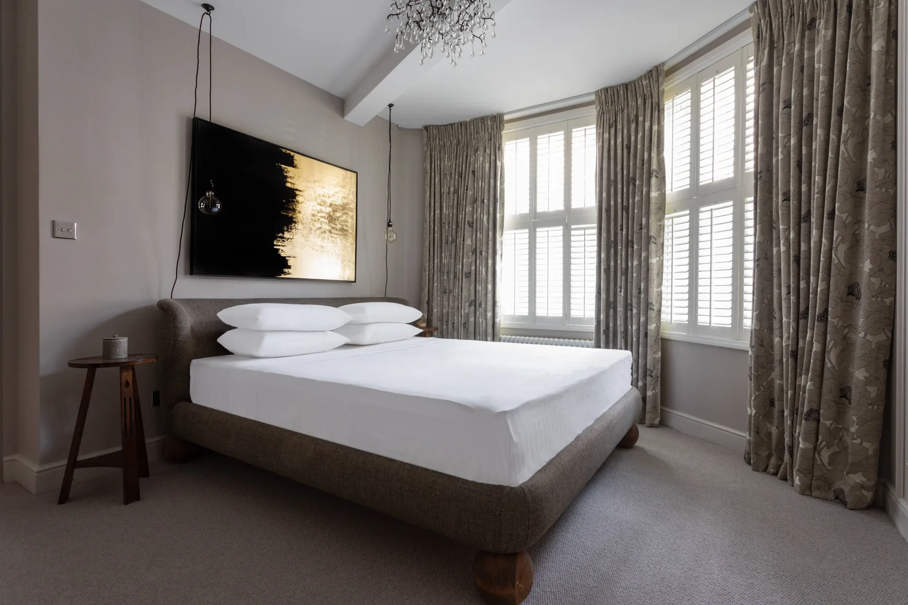 A bedroom with a neatly made bed and tall curtained windows.