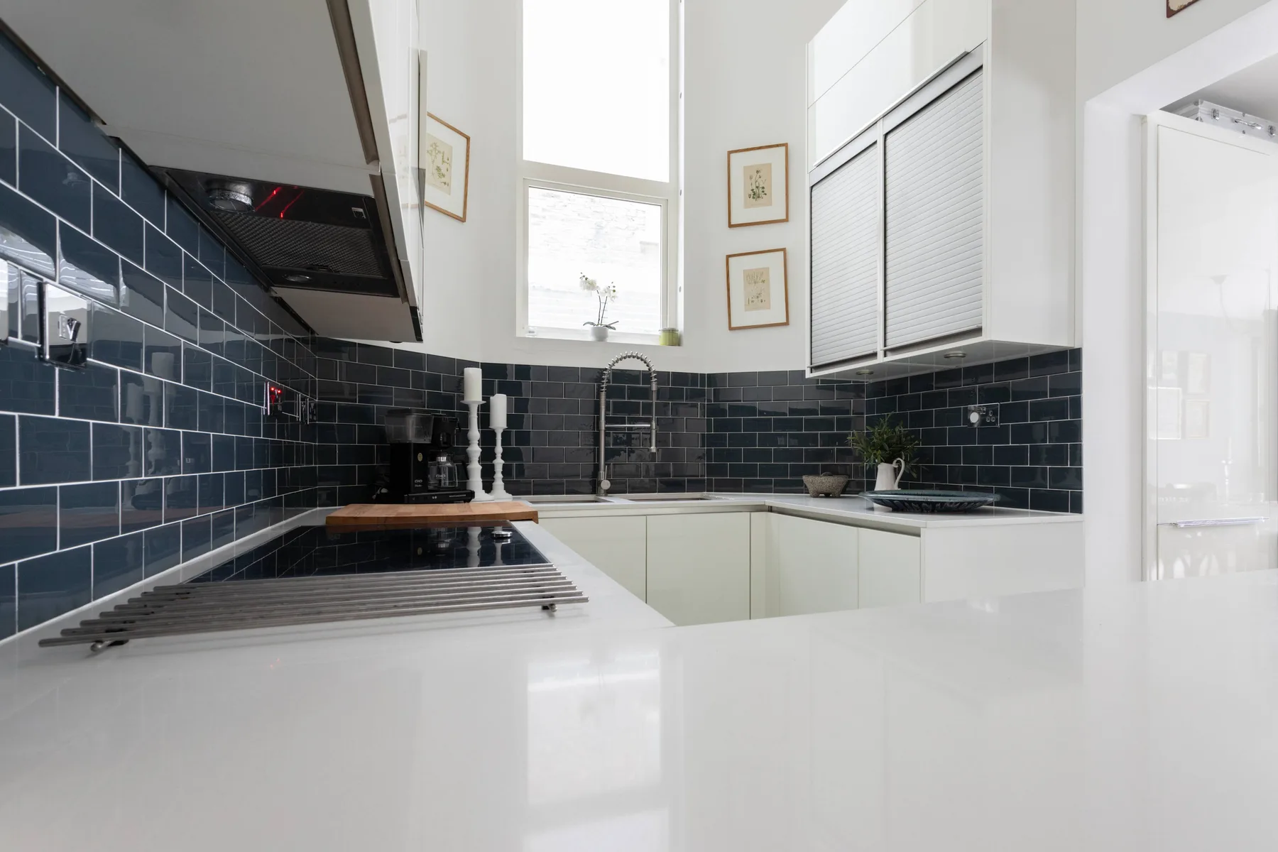 A bright kitchen with dark tiled walls and white countertops.
