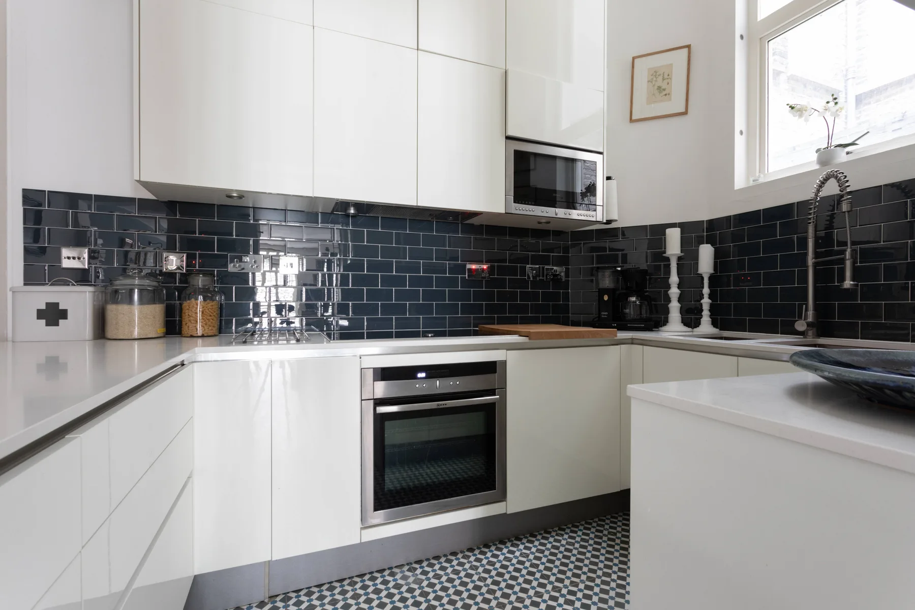 A bright modern kitchen with white cabinets, dark tiled backsplash, and built-in appliances.
