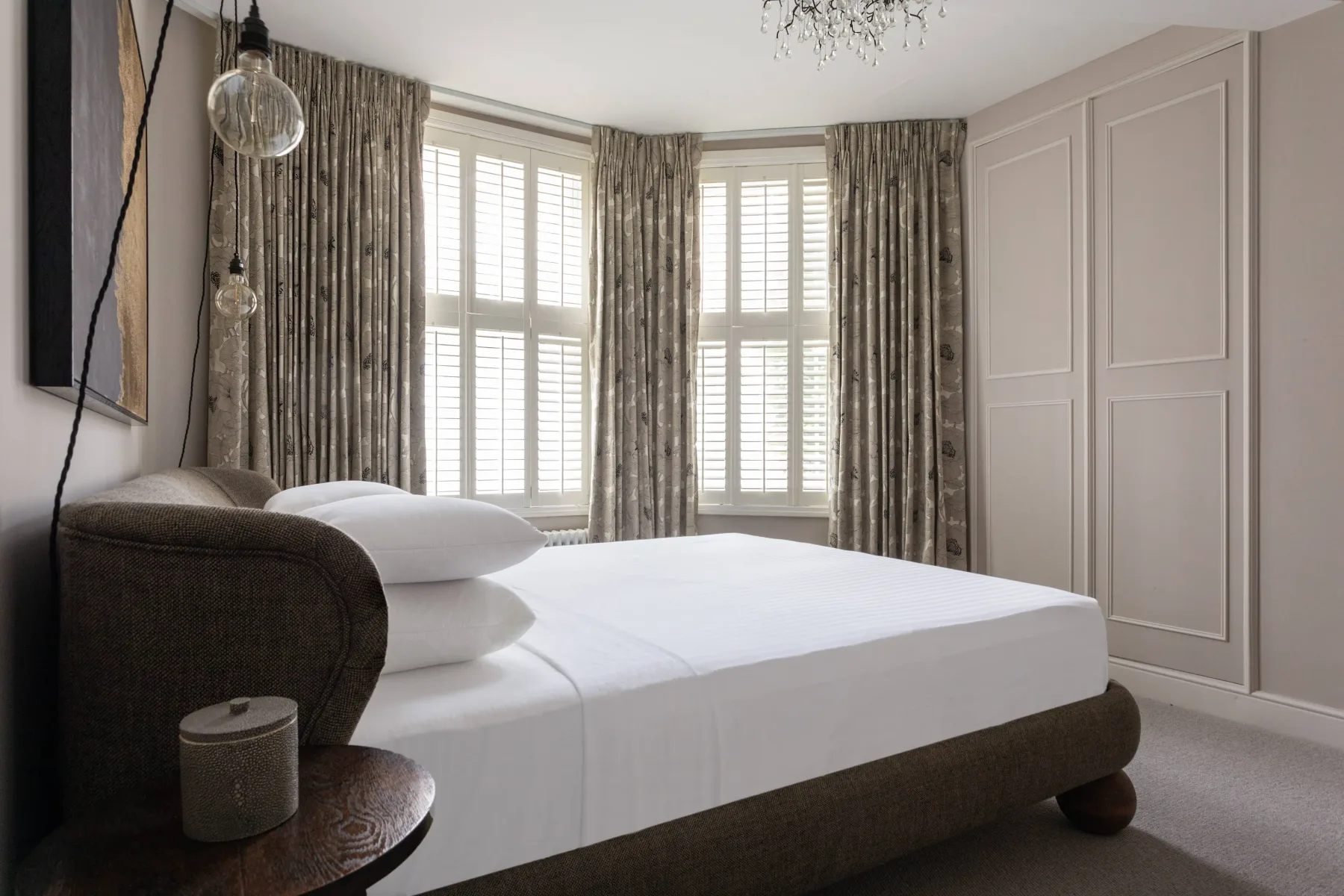 A bedroom with a bed facing tall windows with curtains.