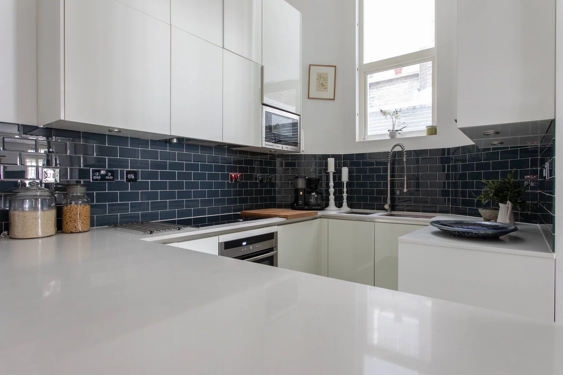 A bright kitchen with white cabinetry, dark tile, and a countertop.
