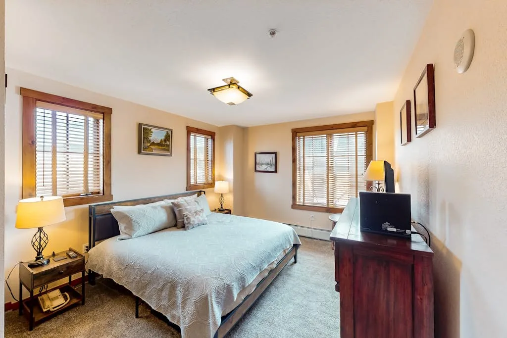 A bedroom with a bed, windows with blinds, and a television on a dresser.