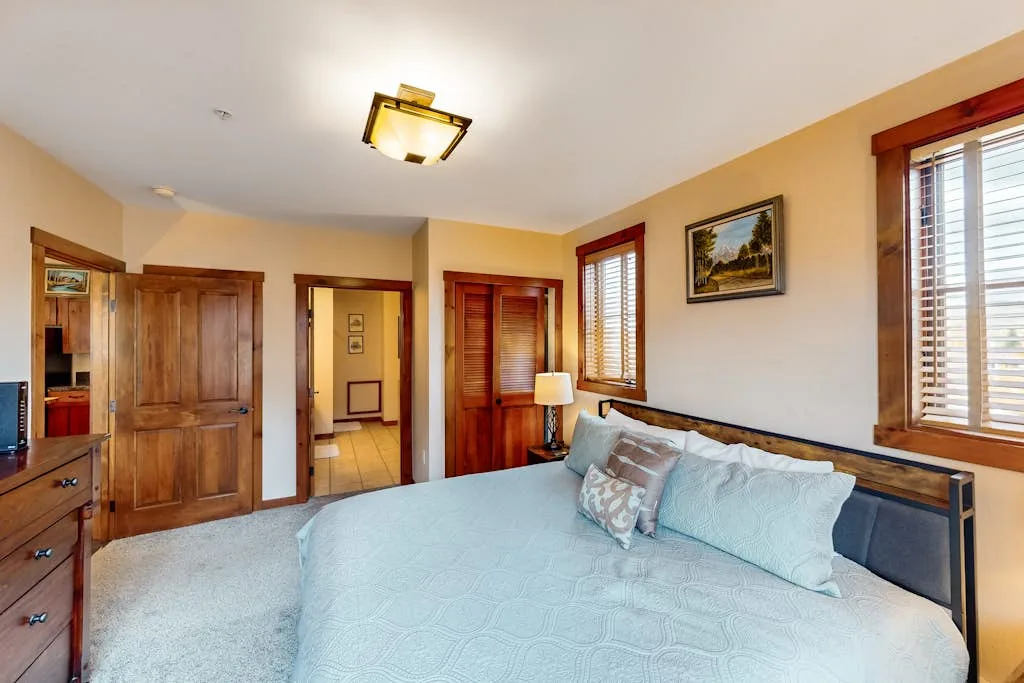 A bedroom with a bed, wooden doors, and windows with blinds.