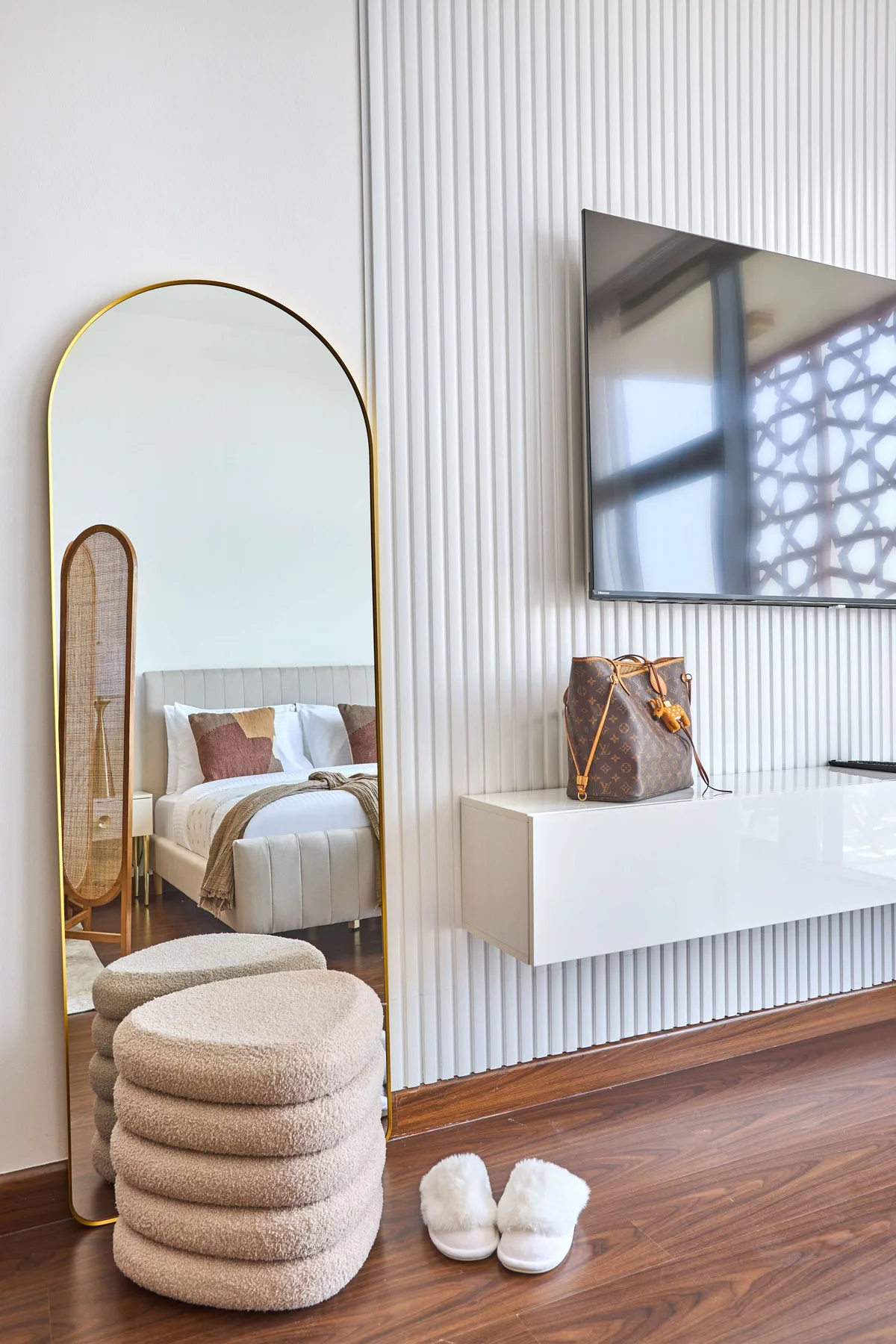 A bedroom seating area features a wall-mounted television and a tall arched mirror.