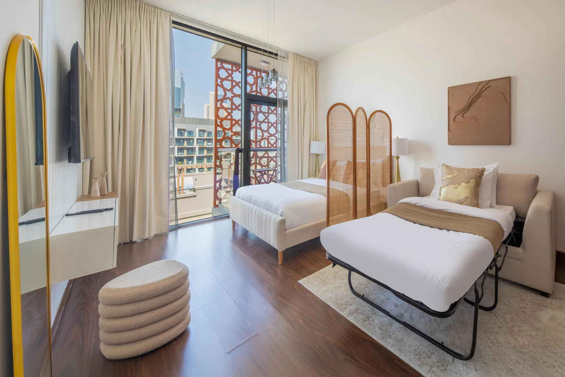 A bright bedroom with two beds, a folding screen, and a glass balcony door.