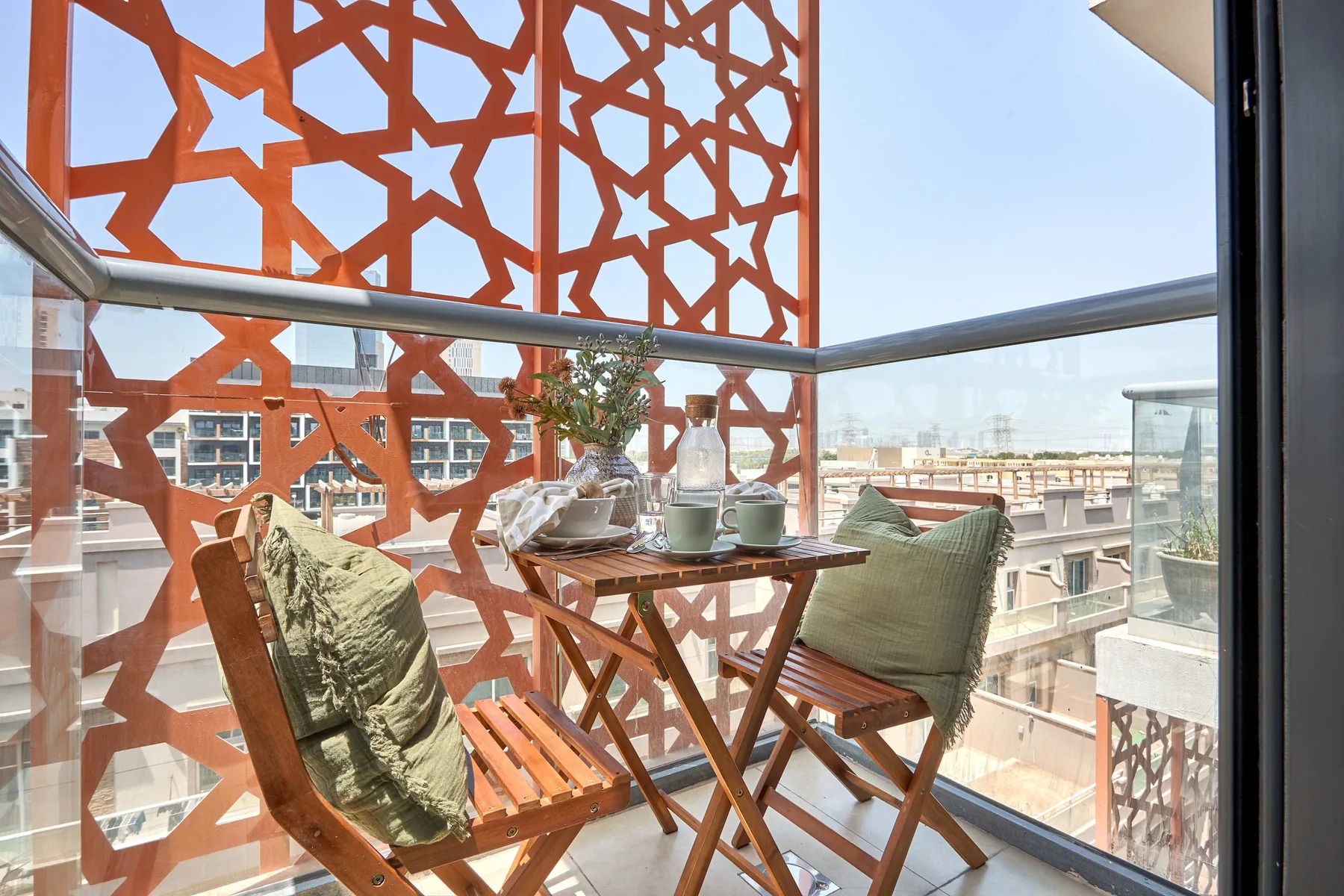 A small balcony with wooden seating and a table overlooks nearby buildings.