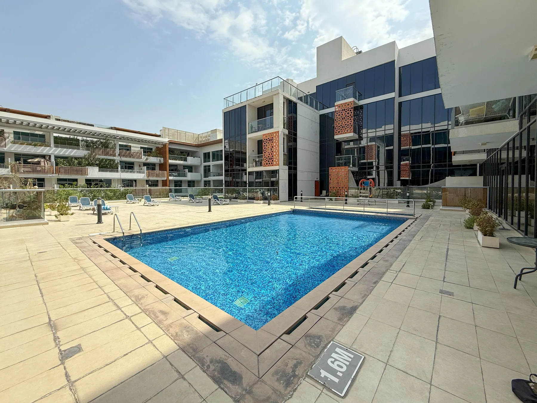 An outdoor swimming pool sits in a paved courtyard surrounded by modern buildings.