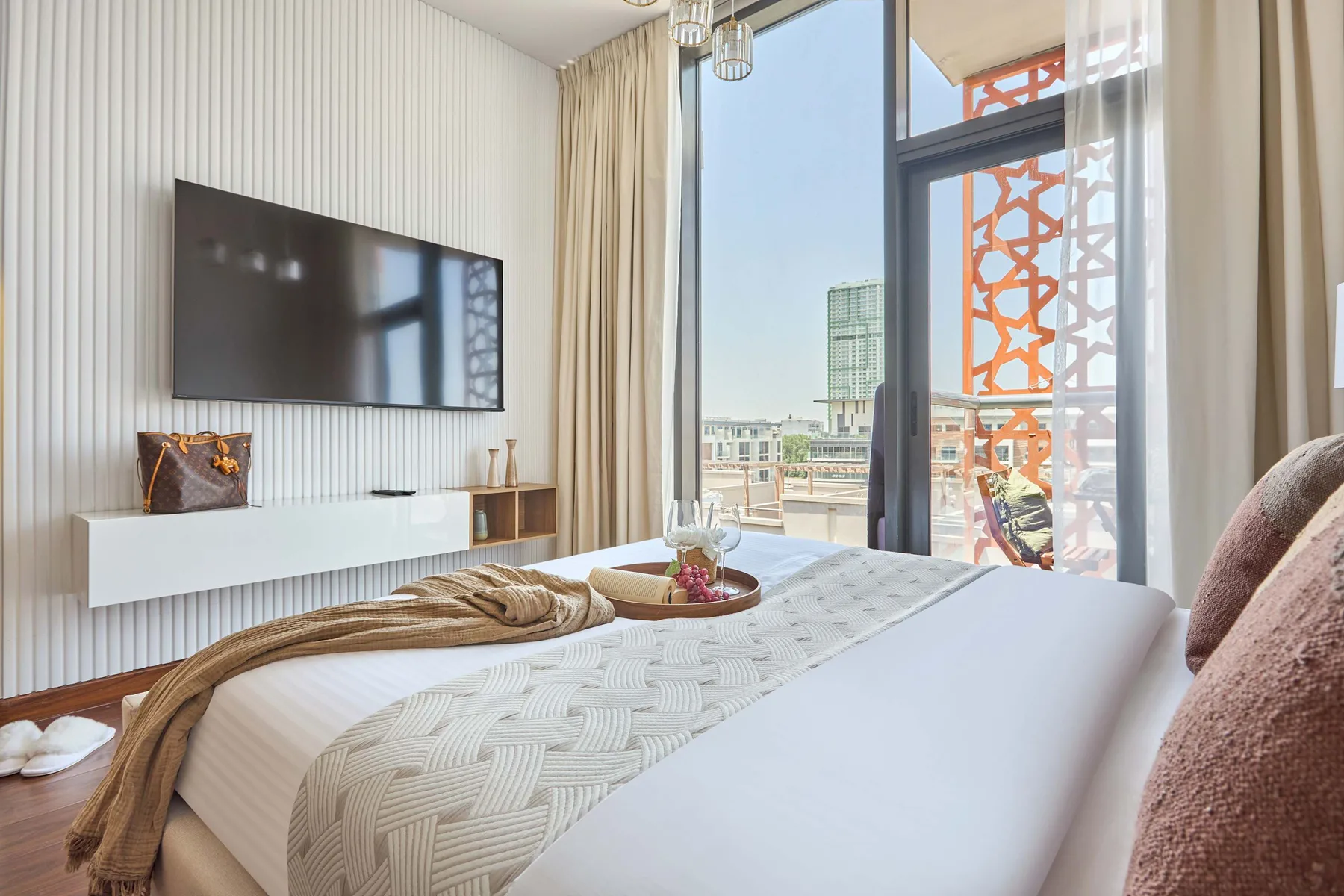 A bright bedroom with a neatly made bed beside floor-to-ceiling windows.