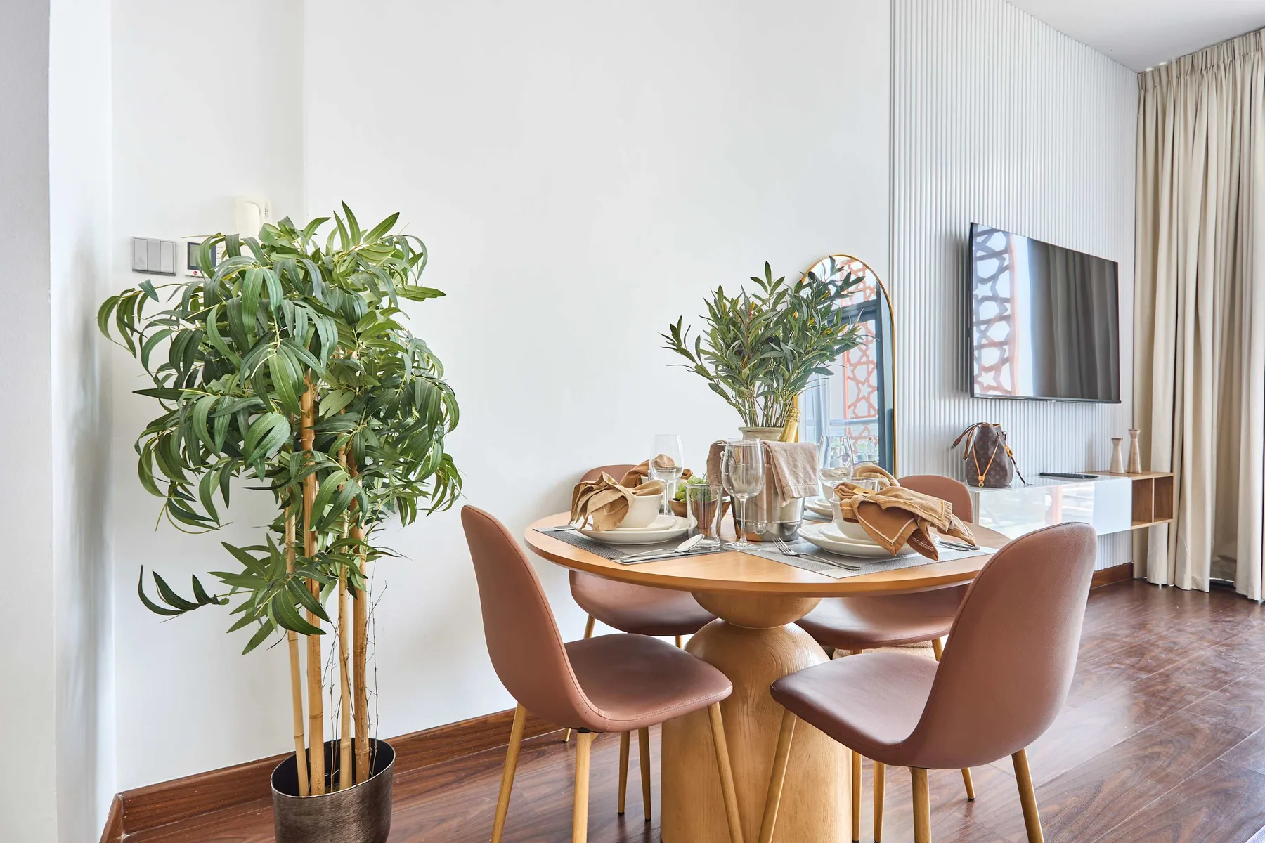A dining area with a round table set with dishes and surrounded by plants.