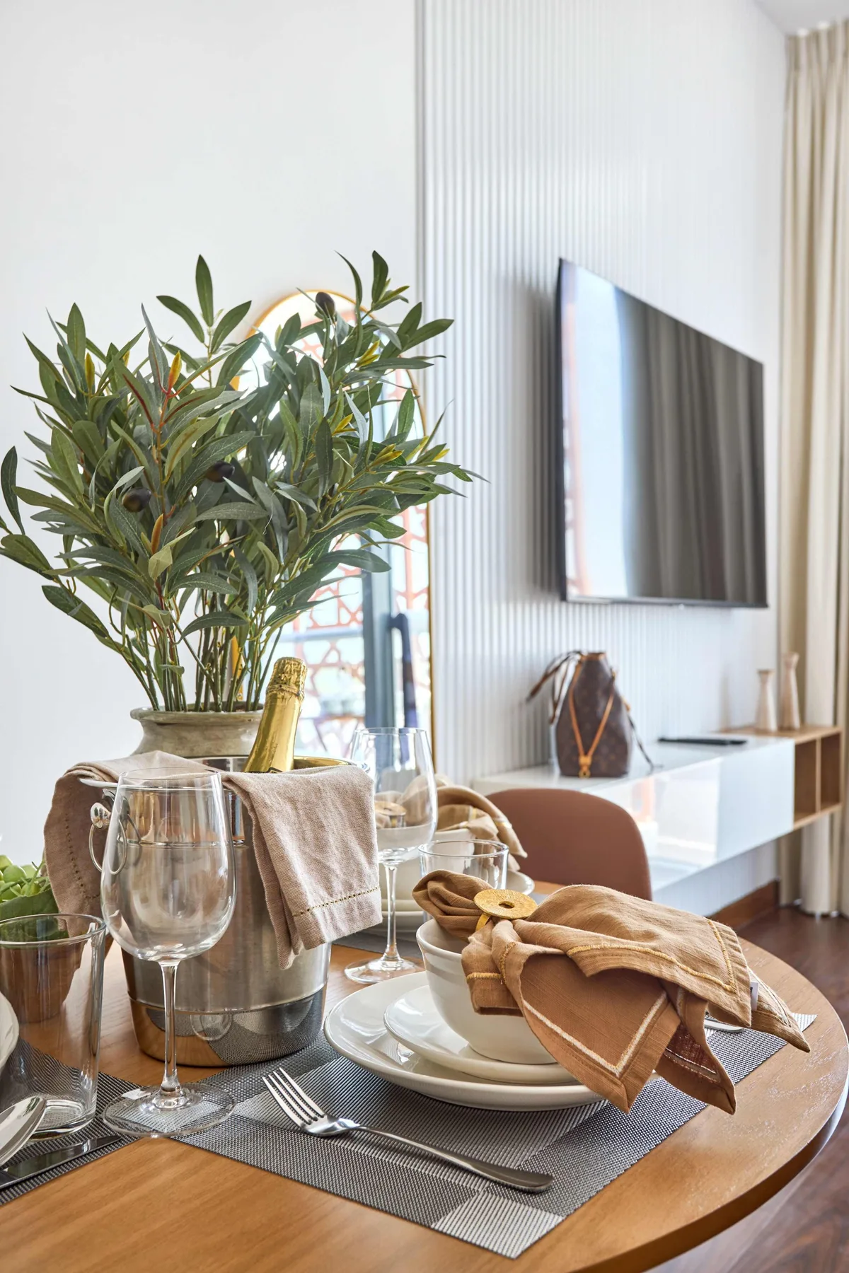 A dining table is set with dishes and folded napkins beside a leafy plant.