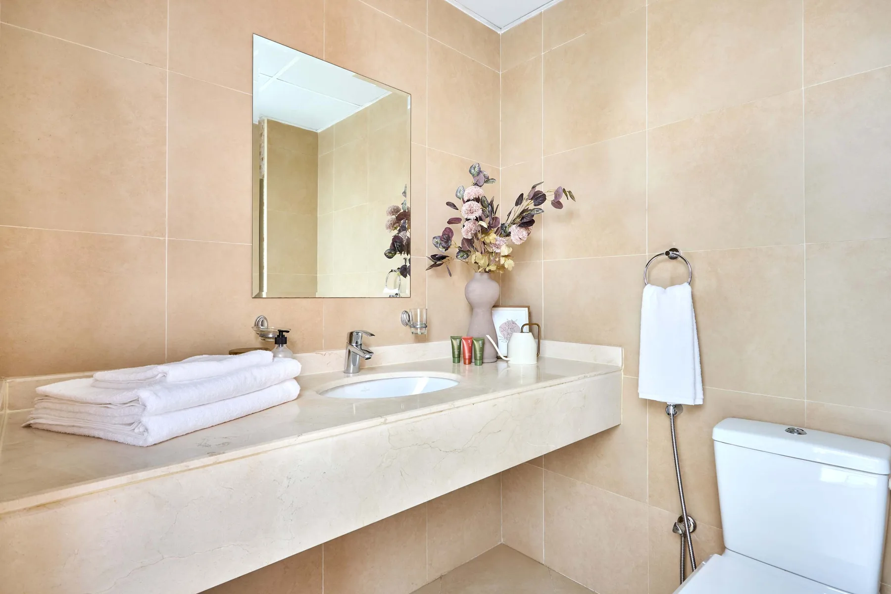 A tiled bathroom with a long sink counter, mirror, and toilet.