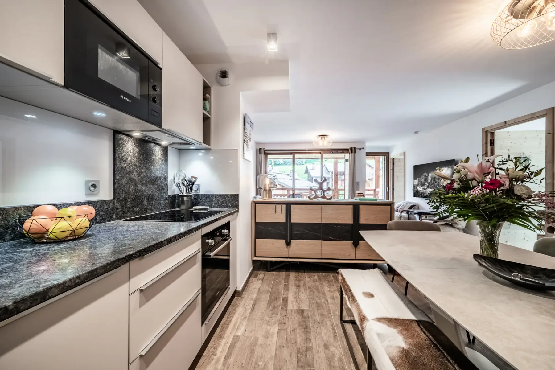 Modern kitchen with white cabinets, black granite countertops, built-in appliances, wooden flooring, and overhead lighting.
