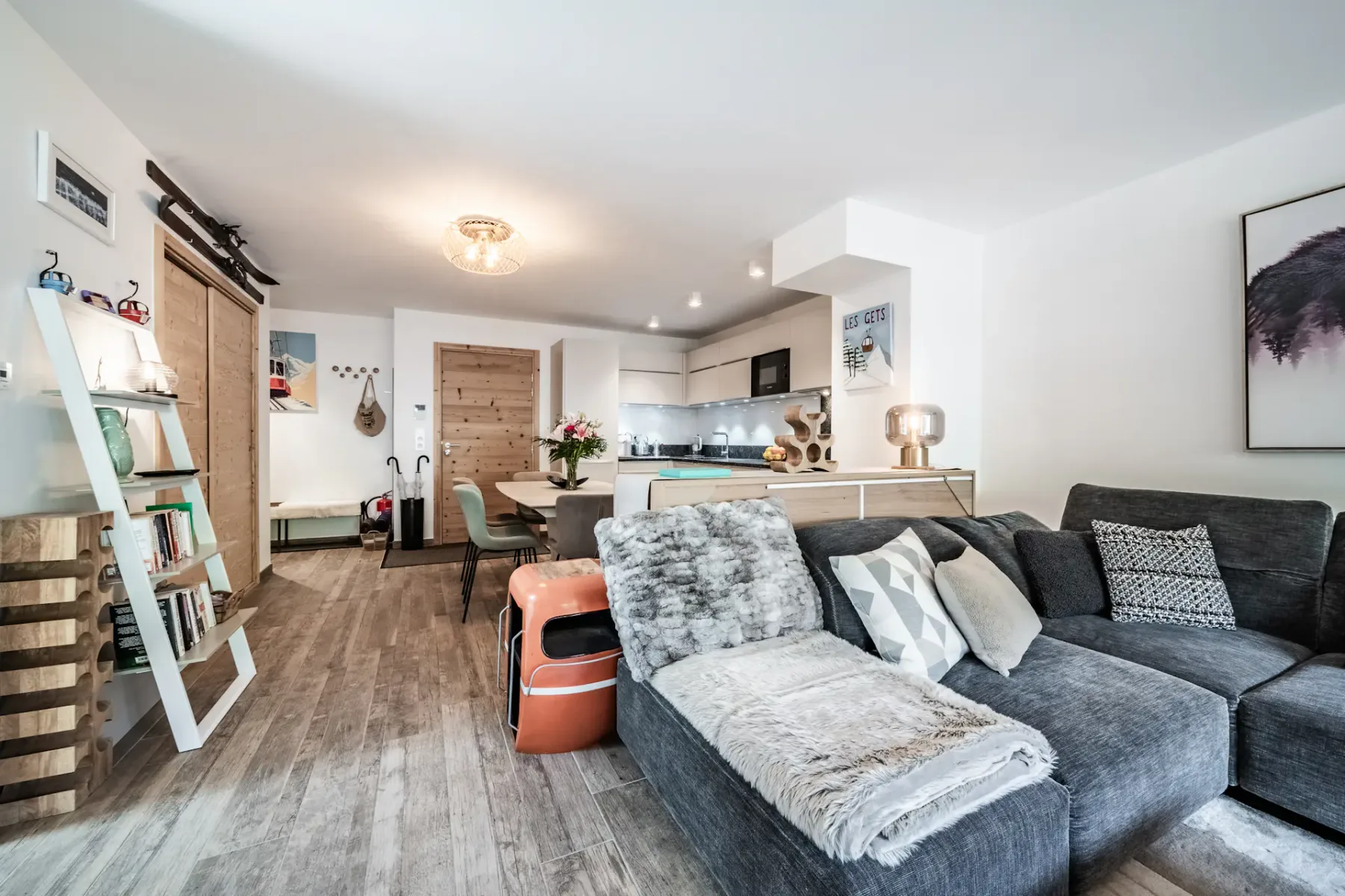 Stylish living room with plush seating, modern decor, large artwork, and a glass door leading to a wooden balcony with a scenic view.