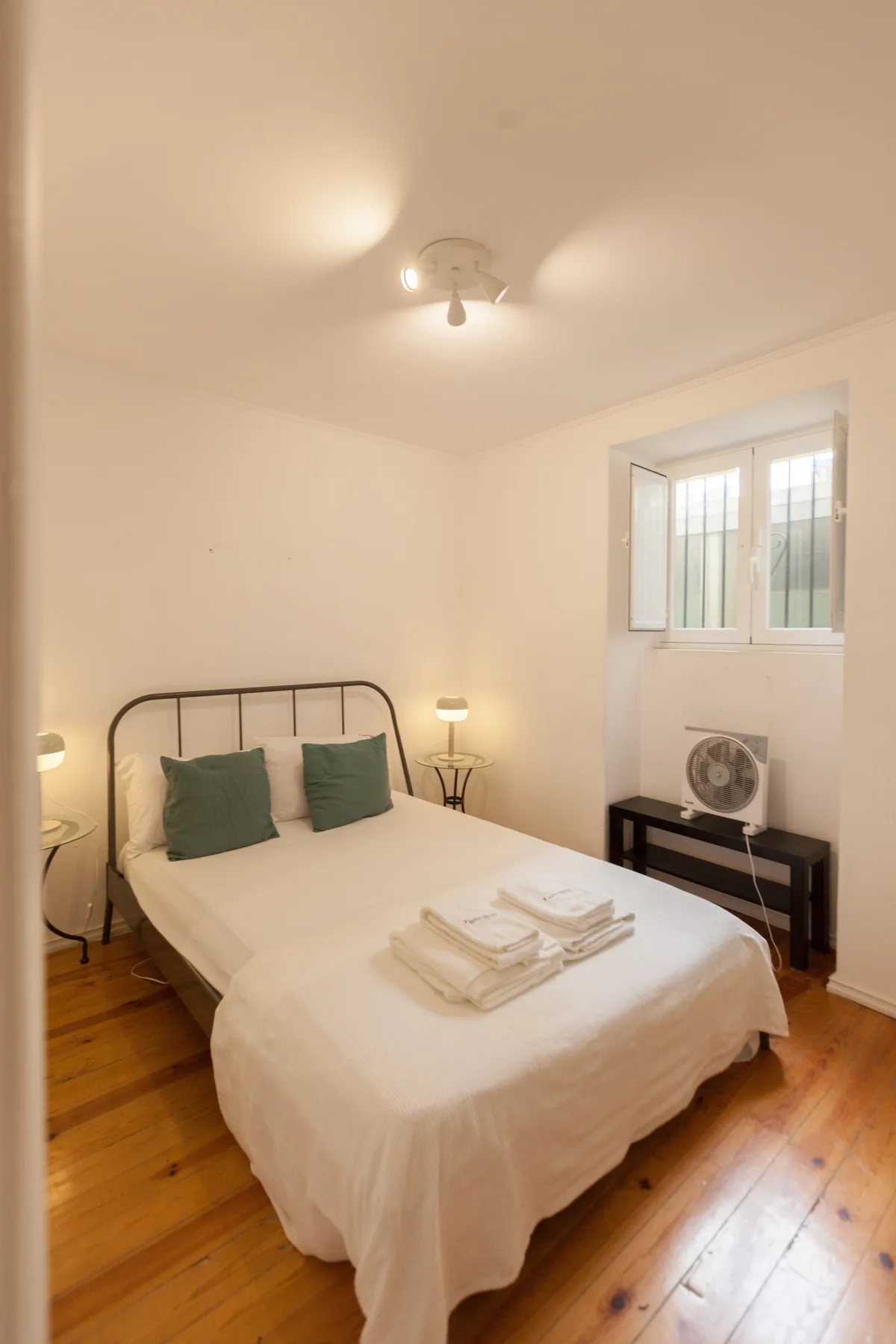 Un dormitorio con una cama, lámparas de noche y una ventana sobre una mesa pequeña.