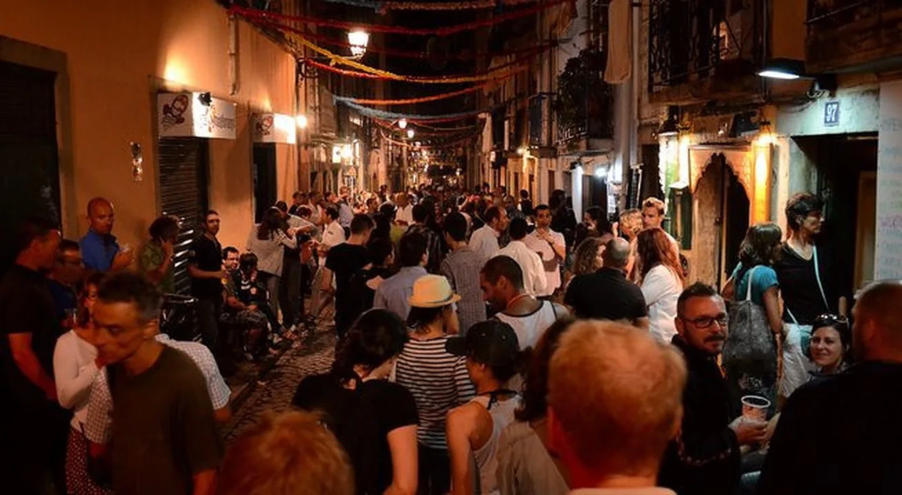 Una calle peatonal concurrida de noche, con gente reunida bajo guirnaldas decorativas.