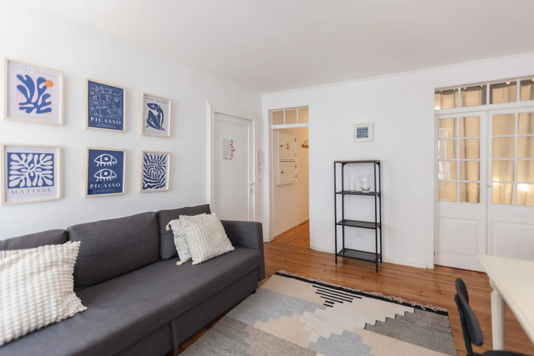 Sala de estar con un sofá gris, láminas enmarcadas y suelo de madera.