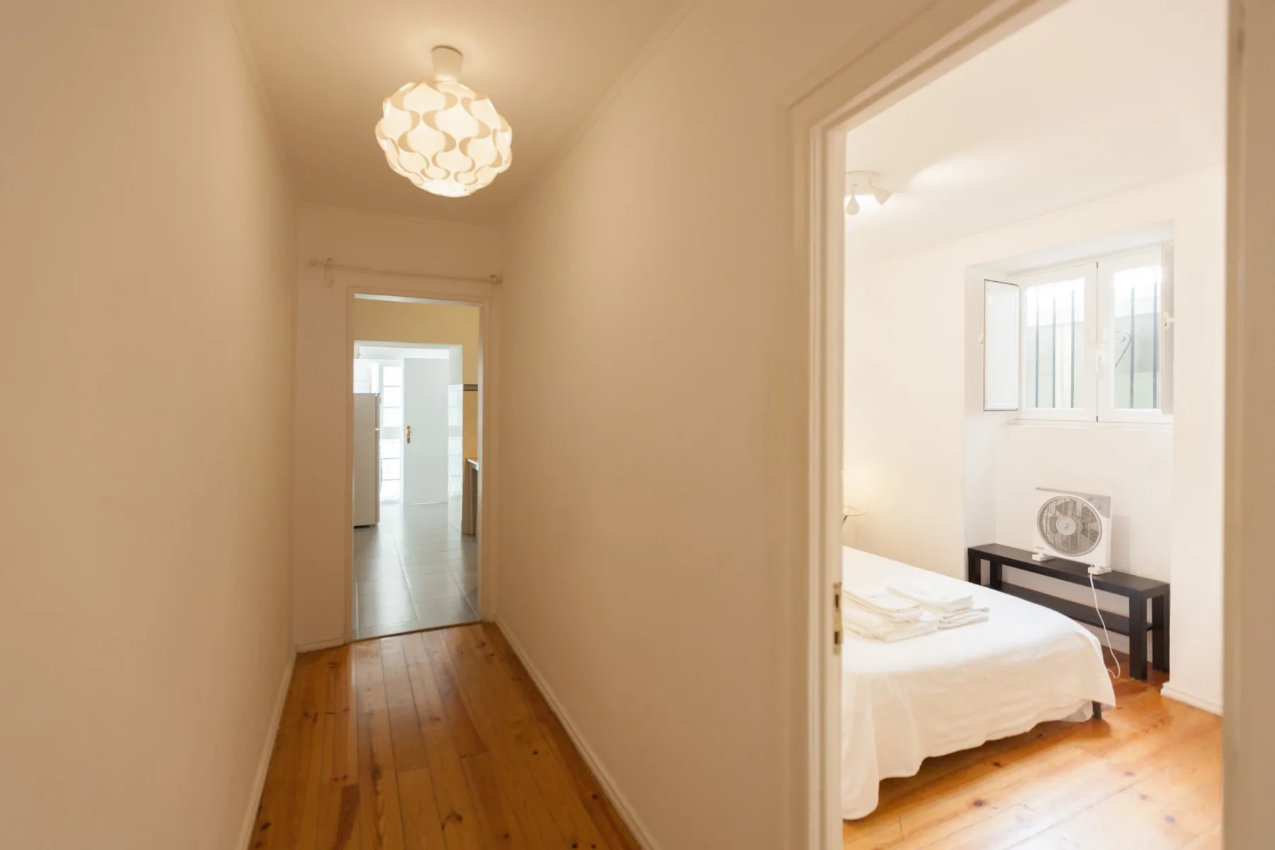Un pasillo estrecho da a un dormitorio luminoso con una cama y una ventana.