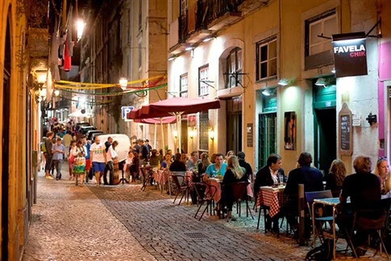 Una calle estrecha adoquinada con mesas de café al aire libre y peatones.