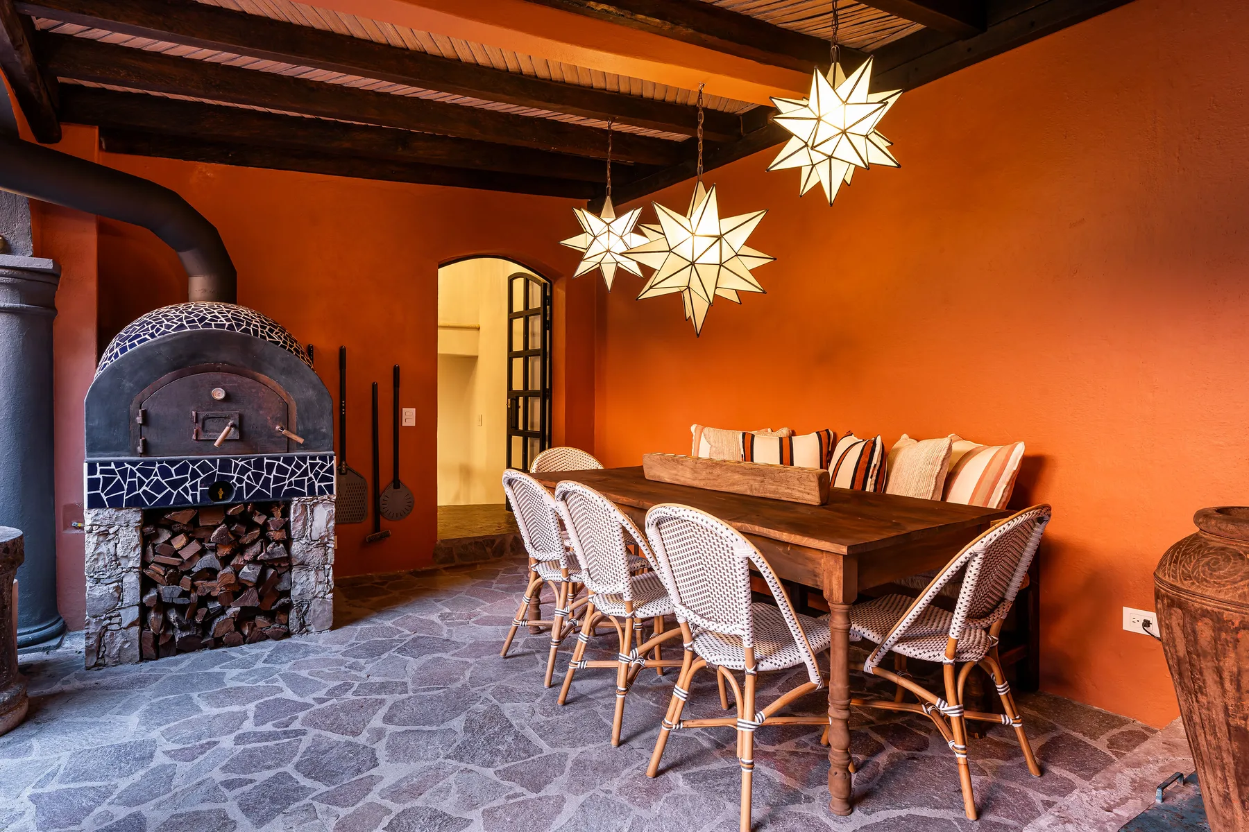 A dining area with a wooden table, woven seating, and a stone fireplace.
