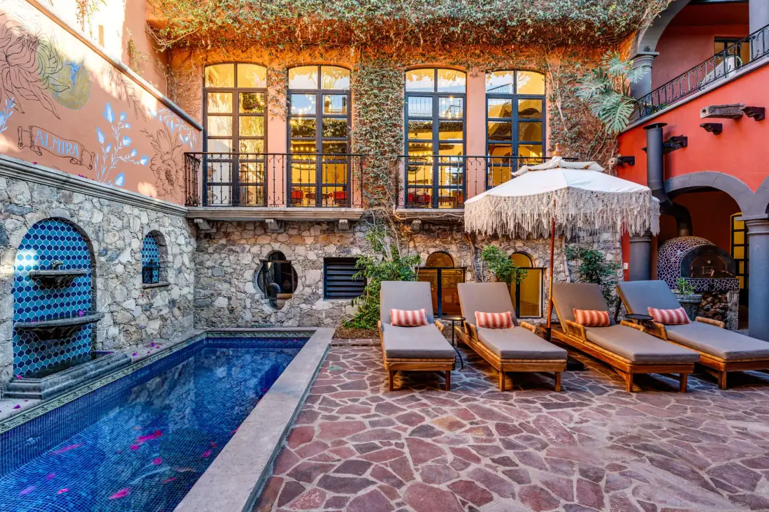A courtyard pool area features lounge seating beneath a large patio umbrella.