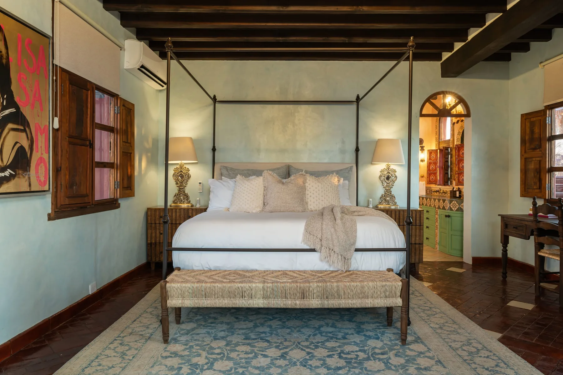 A bedroom with a four-poster bed, bedside lamps, and a patterned rug.