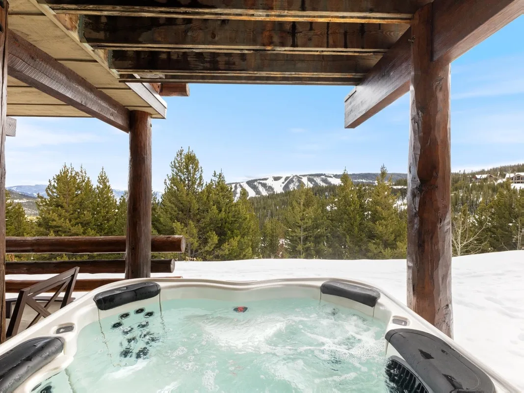 Una bañera de hidromasaje exterior cubierta ofrece vistas a montañas nevadas y arboladas.